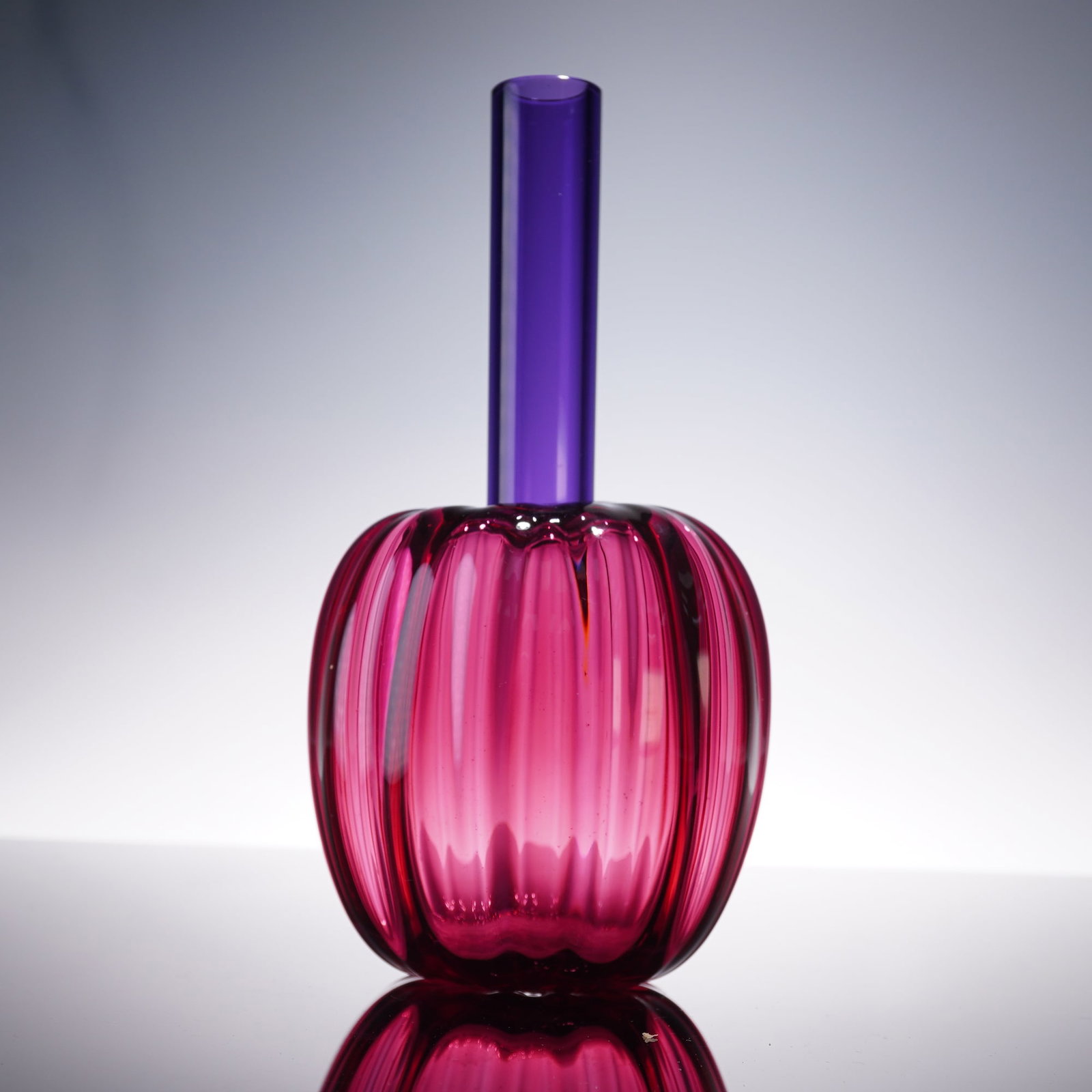 Chatham Glass Co. Jewel Bud Vase, JB 200: Hand-blown art glass in a striking jewel-toned palette, featuring a ribbed cranberry body with vibrant optical depth and a contrasting elongated cylindrical neck in deep amethyst. The piece showcases 