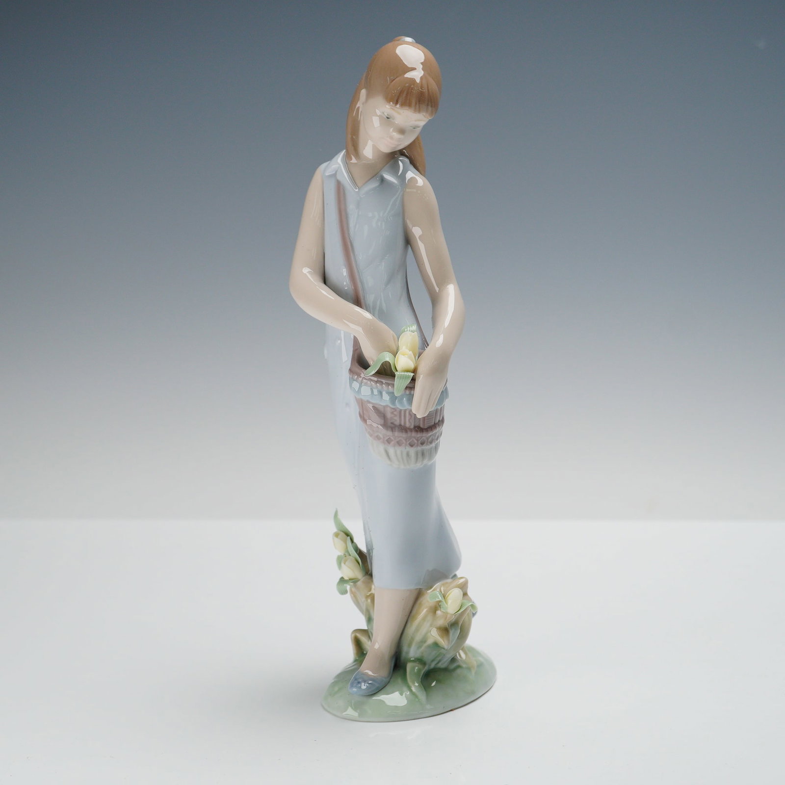 Lladro Porcelain Figurine, Tulip Garden 1007712: A graceful Lladro porcelain figurine titled Tulip Garden (model number 1007712), released in 2007 as the Annual Privilege Piece. It depicts a young girl in a pale blue dress carrying a basket of fresh