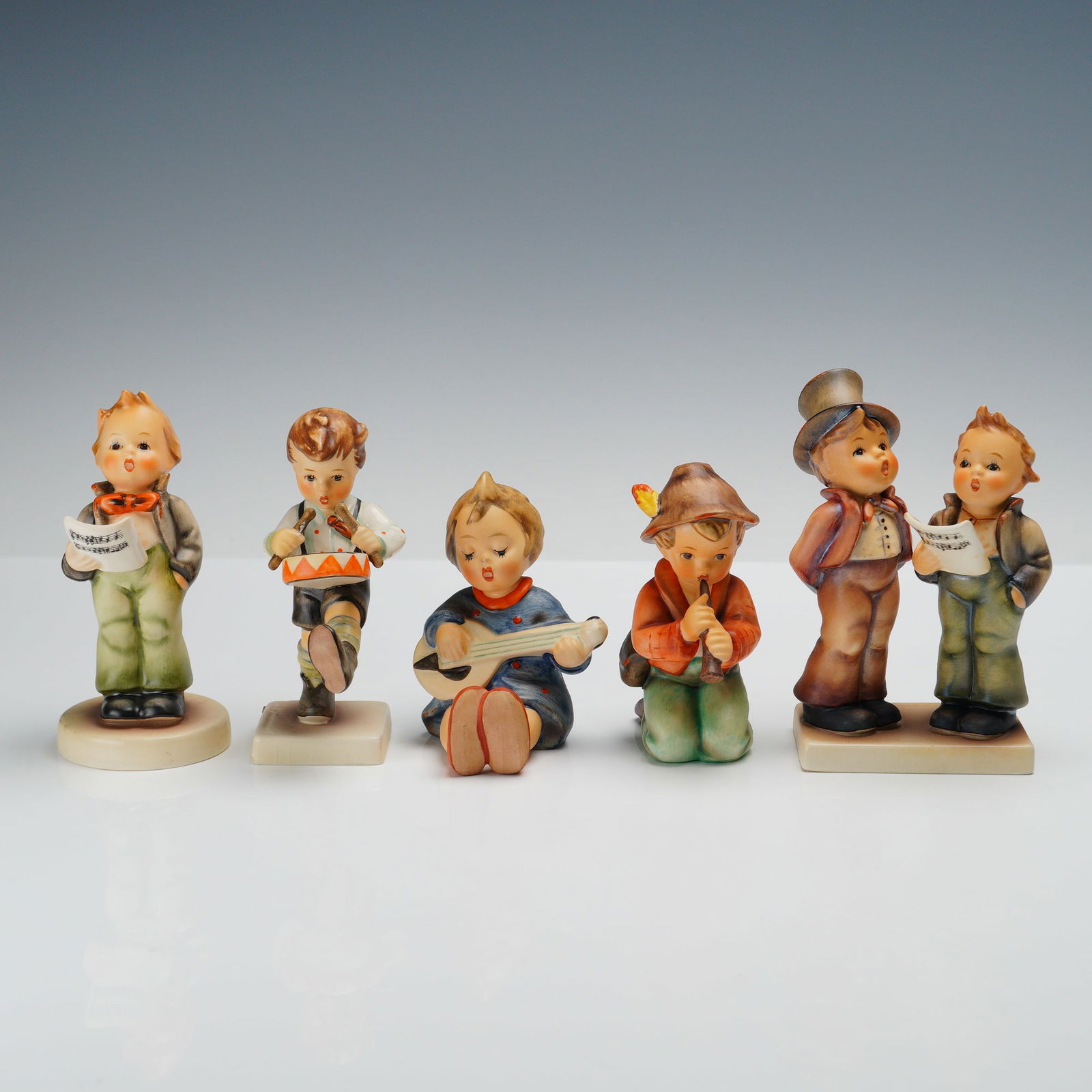 5pc Goebel Hummel Musical Themed Figurines: A charming group of five Goebel Hummel figurines, each capturing a musical theme. Duet features two boys singing together from a shared music sheet, one wearing a tall top hat. Little Drummer is a you