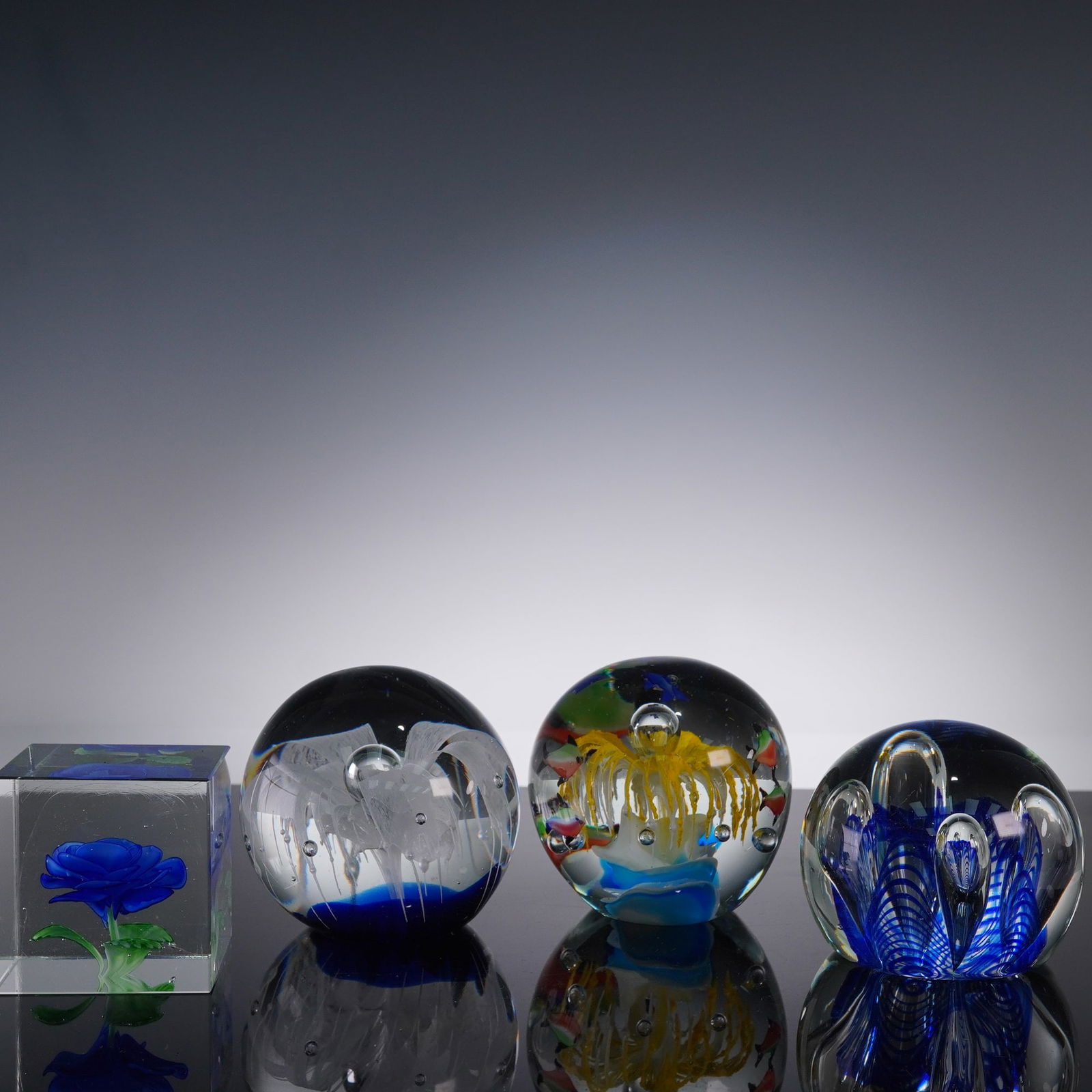4pc Art Glass Paperweight Collection Round Cube Flower: This collection features four beautifully crafted art glass paperweights. The round pieces include one with a colorful aquarium design, complete with fish; one with a white lacy fountain and controlle