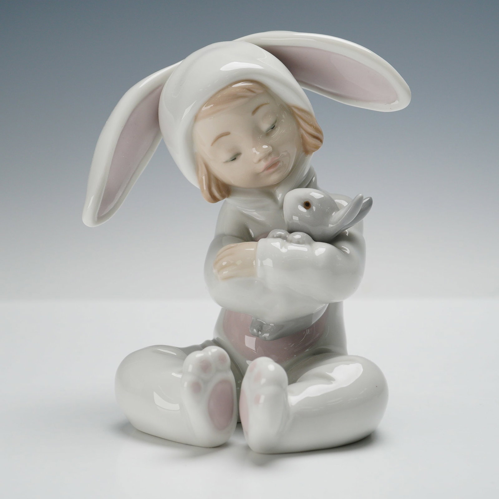 Lladro Porcelain Figurine, Bunny Hugs 01008538: Lladro porcelain figurine titled Bunny Hugs (01008538), designed by Jose Javier Malavia. This heartwarming piece features a young child in a charming bunny costume, complete with oversized ears, tende