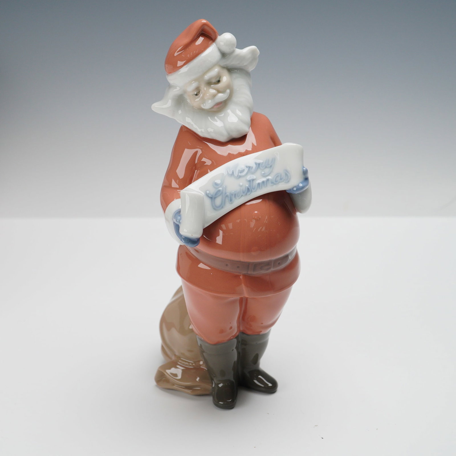 Nao by Lladro Figurine, Santa's Best Wishes 1399: This handcrafted glossy porcelain piece from Spain depicts Santa Claus holding a scroll inscribed with Merry Christmas, with a sack resting behind him. Marked on the underside with the Nao by Lladro s