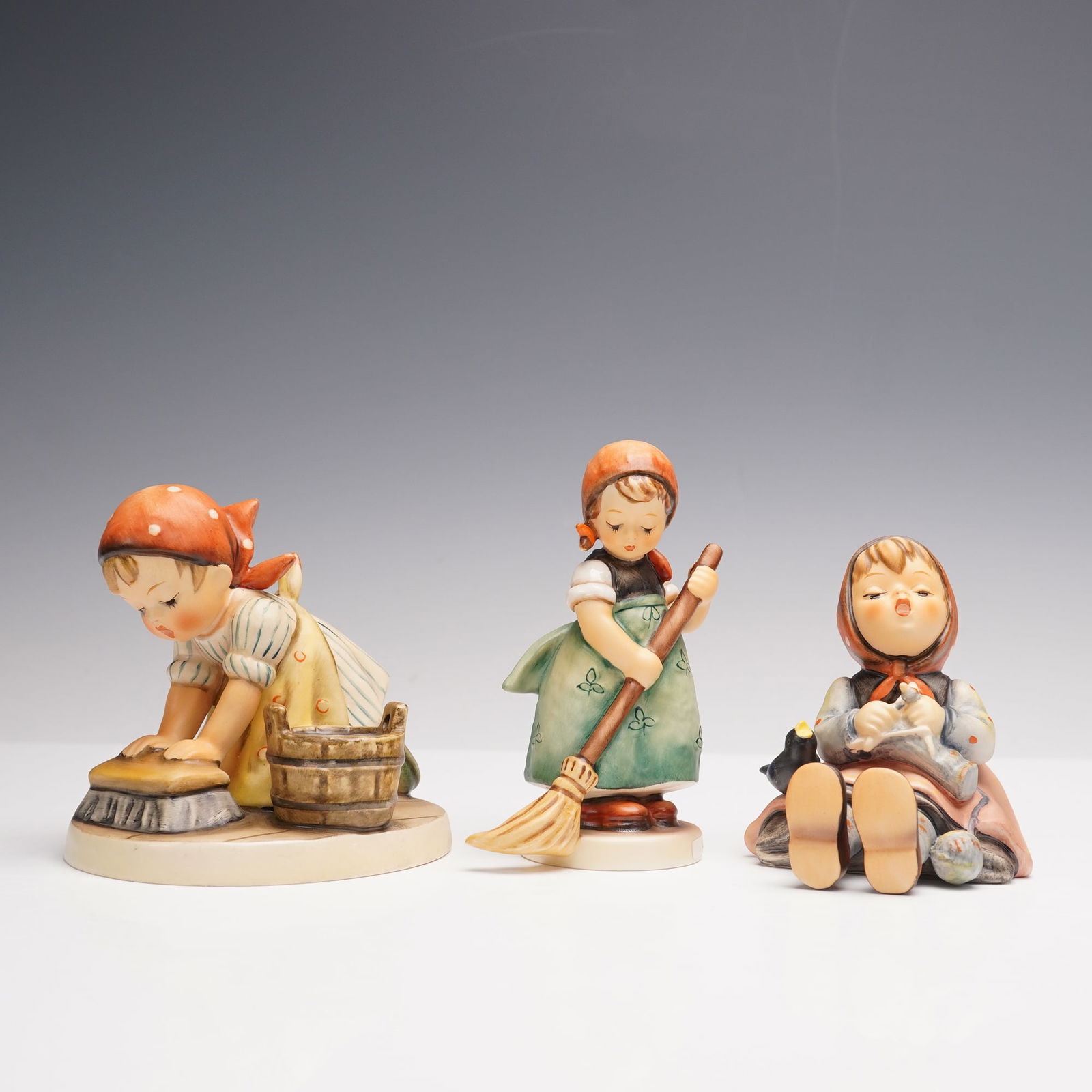 3pc Goebel Hummel Porcelain Figurines: A grouping of three porcelain figures, each depicting young girls engaged in domestic activities. Included are Little Sweeper, Happy Pastime, Housecleaning. M. I. Hummel impressed backstamp. Goebel ba