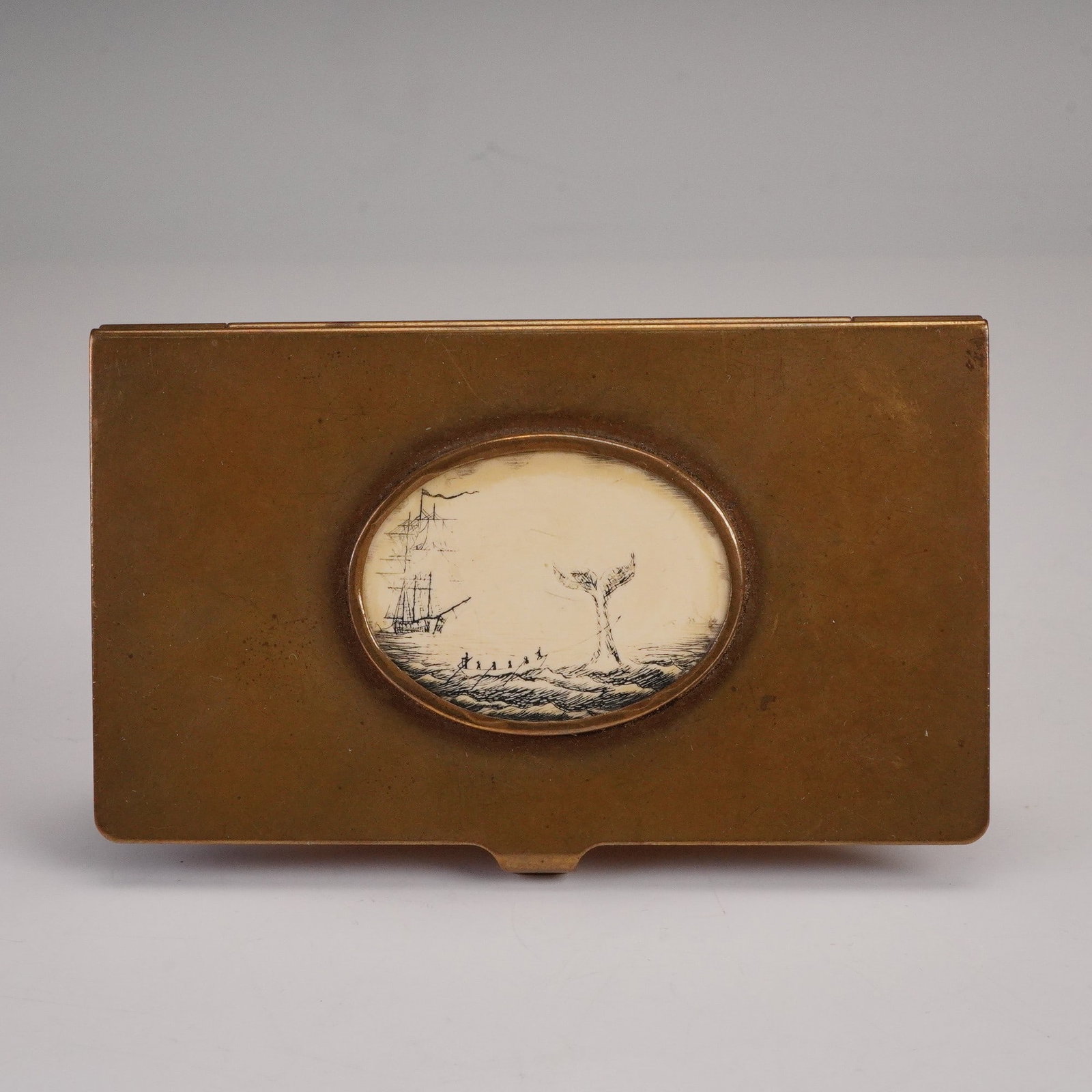 Vintage Brass Card Case with Scrimshaw-Style Plaque: This vintage brass card case features a mounted oval scrimshaw-style plaque depicting a classic maritime whaling scene, with a tall ship, a whaleboat crew, and the flukes of a whale breaching above th