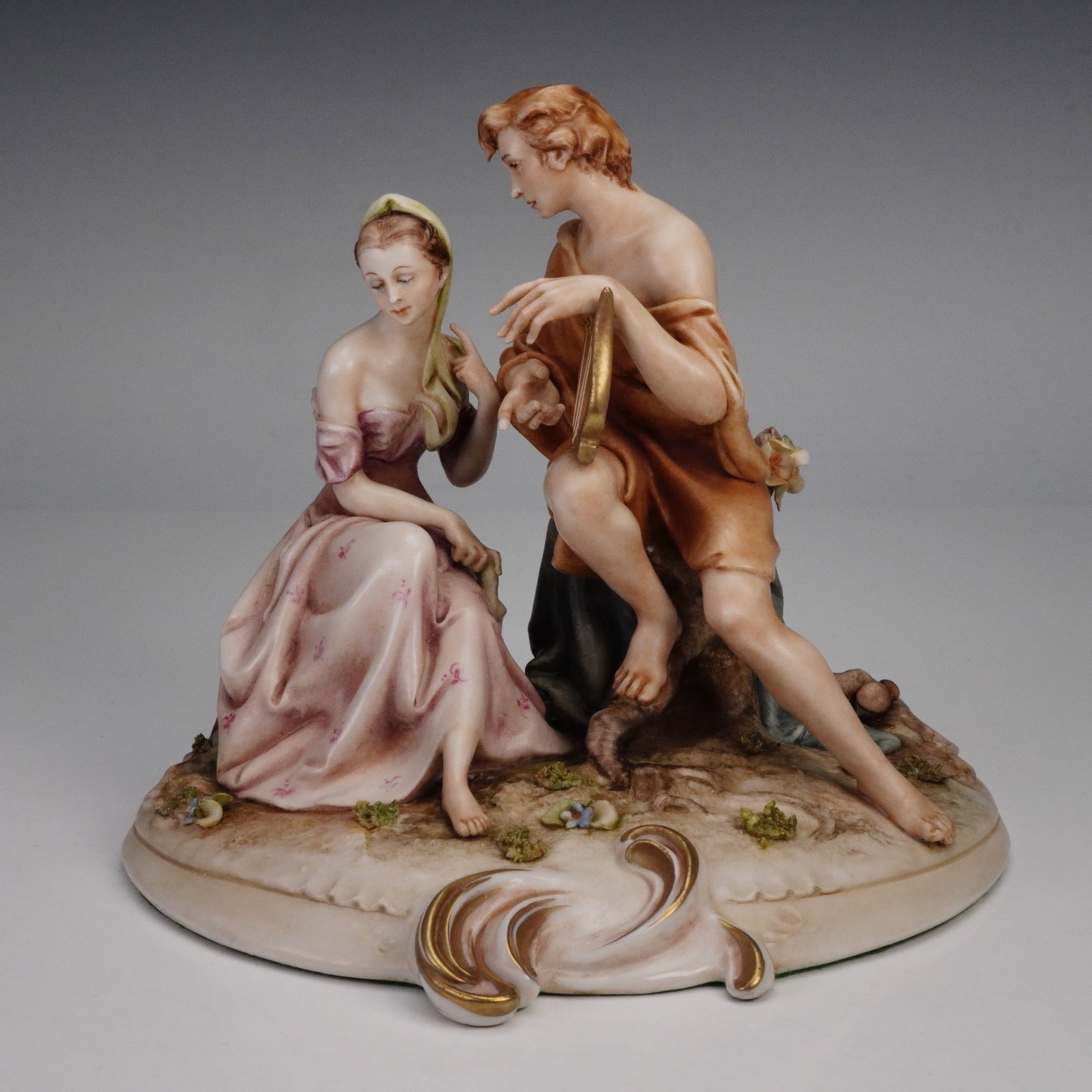 Borsato Figurine, Psyche and Eros 784: Handcrafted Italian porcelain figurine depicting Psyche and Eros seated together in a romantic scene. Psyche is shown in a flowing pink gown with delicate floral details, while Eros, dressed in classi