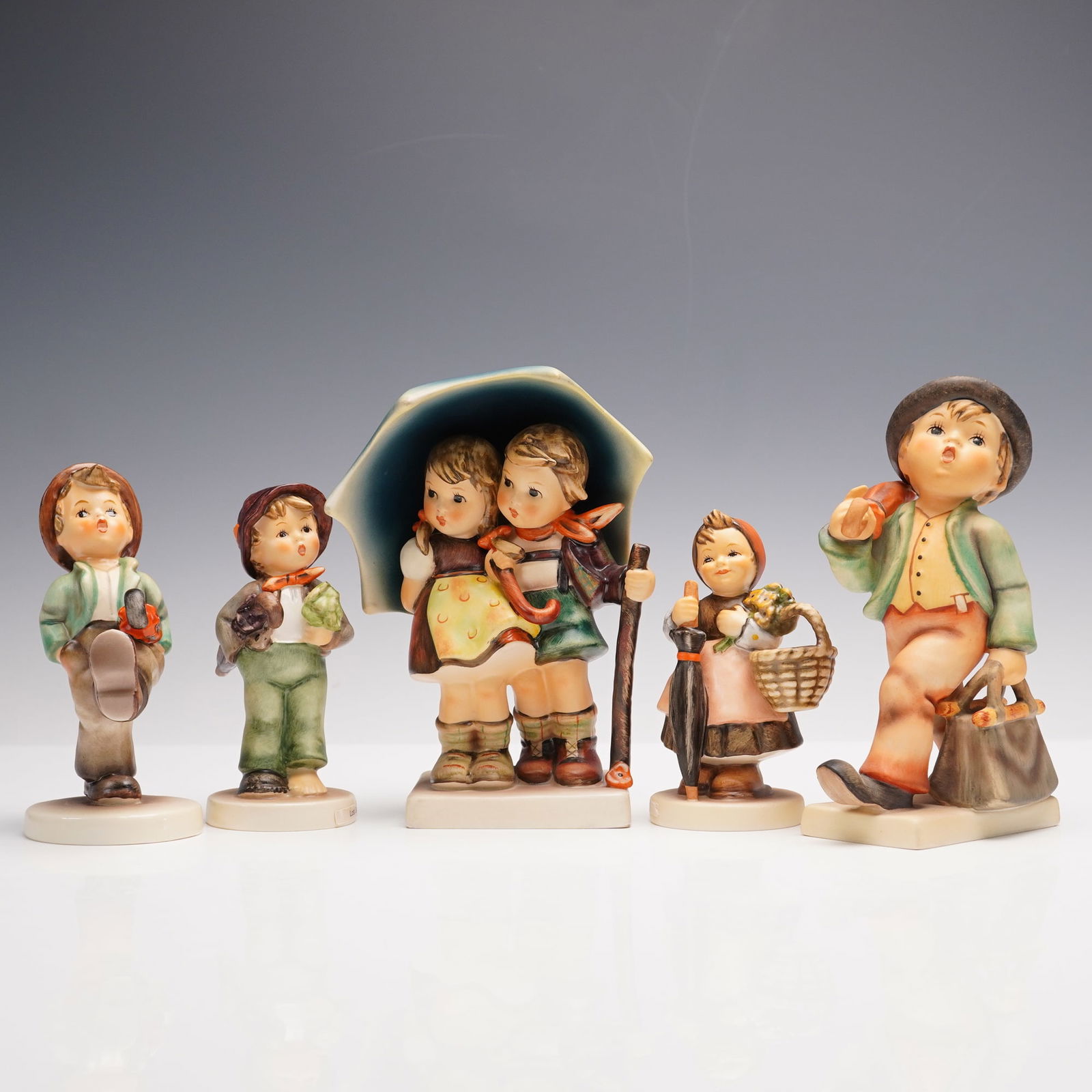 5pc Goebel Hummel Porcelain Figurines: A collection of five porcelain figurines, each hand-painted with fine detail and embodying the pastoral themes for which the series is renowned. The group includes Stormy Weather, Merry Wanderer, On H