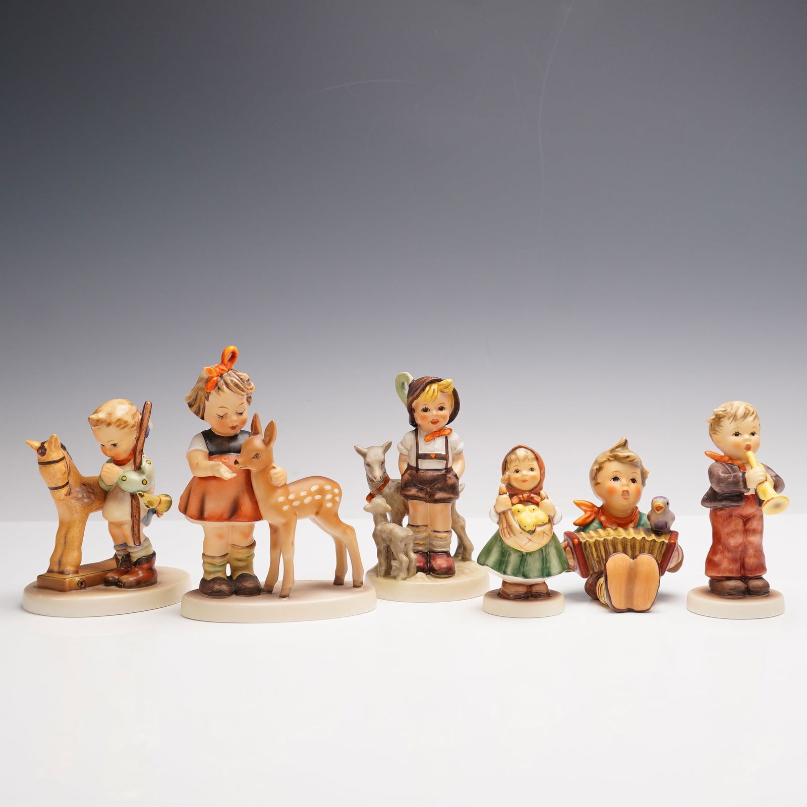 6pc Goebel Hummel Porcelain Figurines: An assorted grouping of six porcelain figurines, each executed with intricate detail and hand-painted decoration characteristic of the celebrated German tradition. This selection features children in