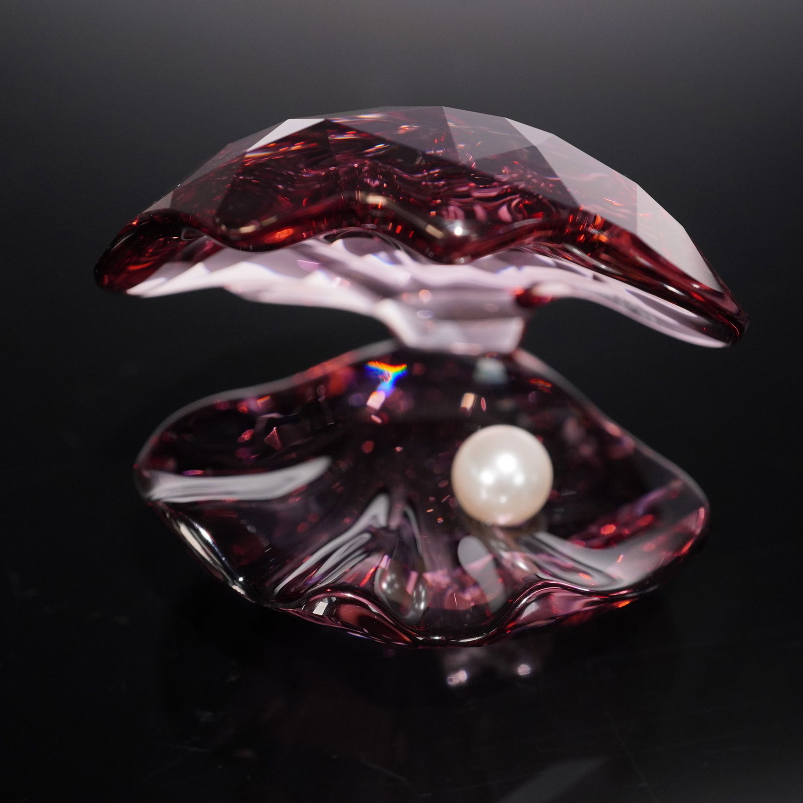 Swarovski Crystal Figurine Pearl Oyster Antique Pink 5035512: Crystal figurine depicting a stylized oyster shell in faceted antique pink crystal, accented with deep red tones and housing a single luminous pearl. Designed with intricate cuts that reflect light be