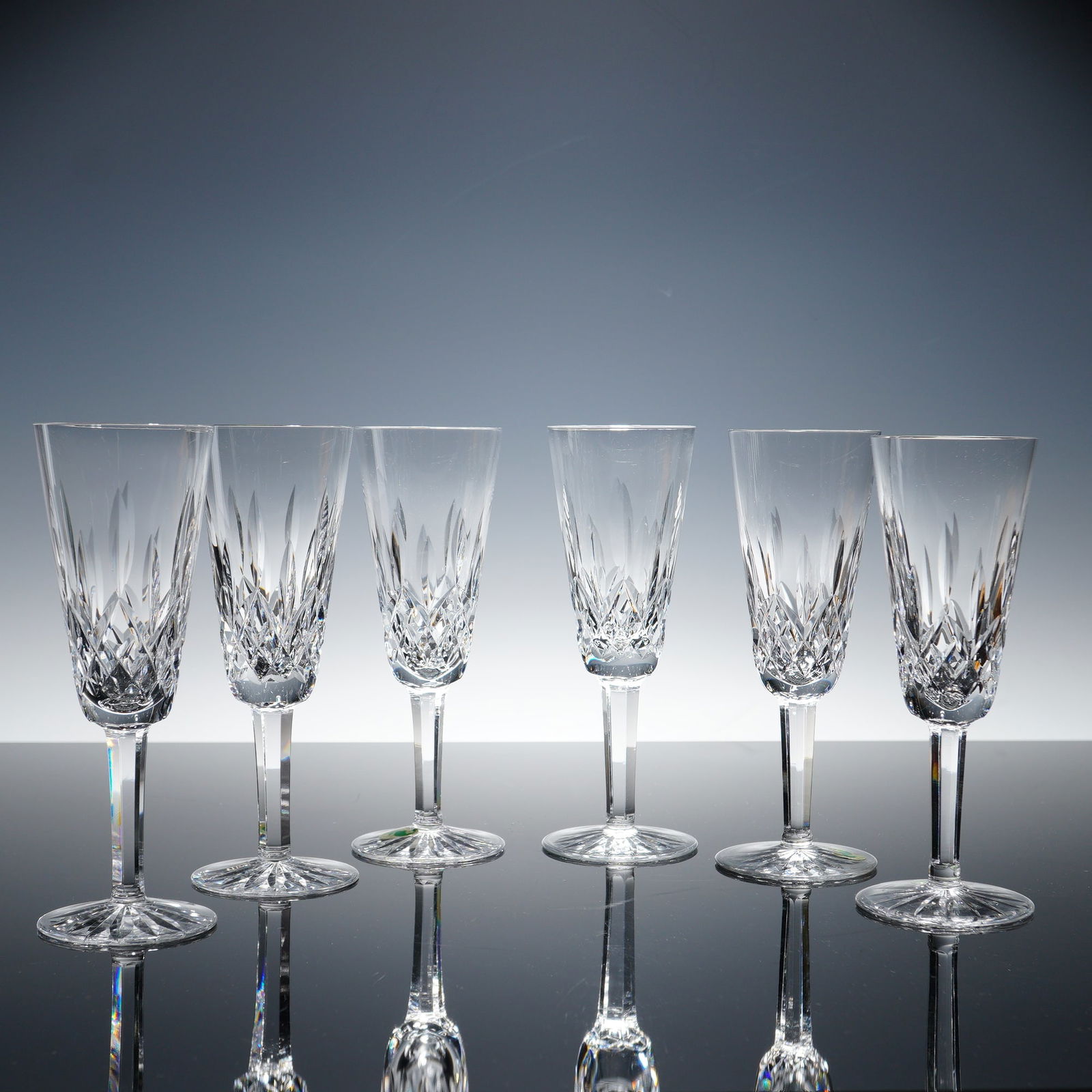 6pc Waterford Lismore Crystal Fluted Champagne Glasses: A set of six crystal fluted champagne glasses in the iconic Lismore pattern. Featuring the classic diamond and wedge cut design, each glass is finely crafted with faceted detail and a starburst cut fo
