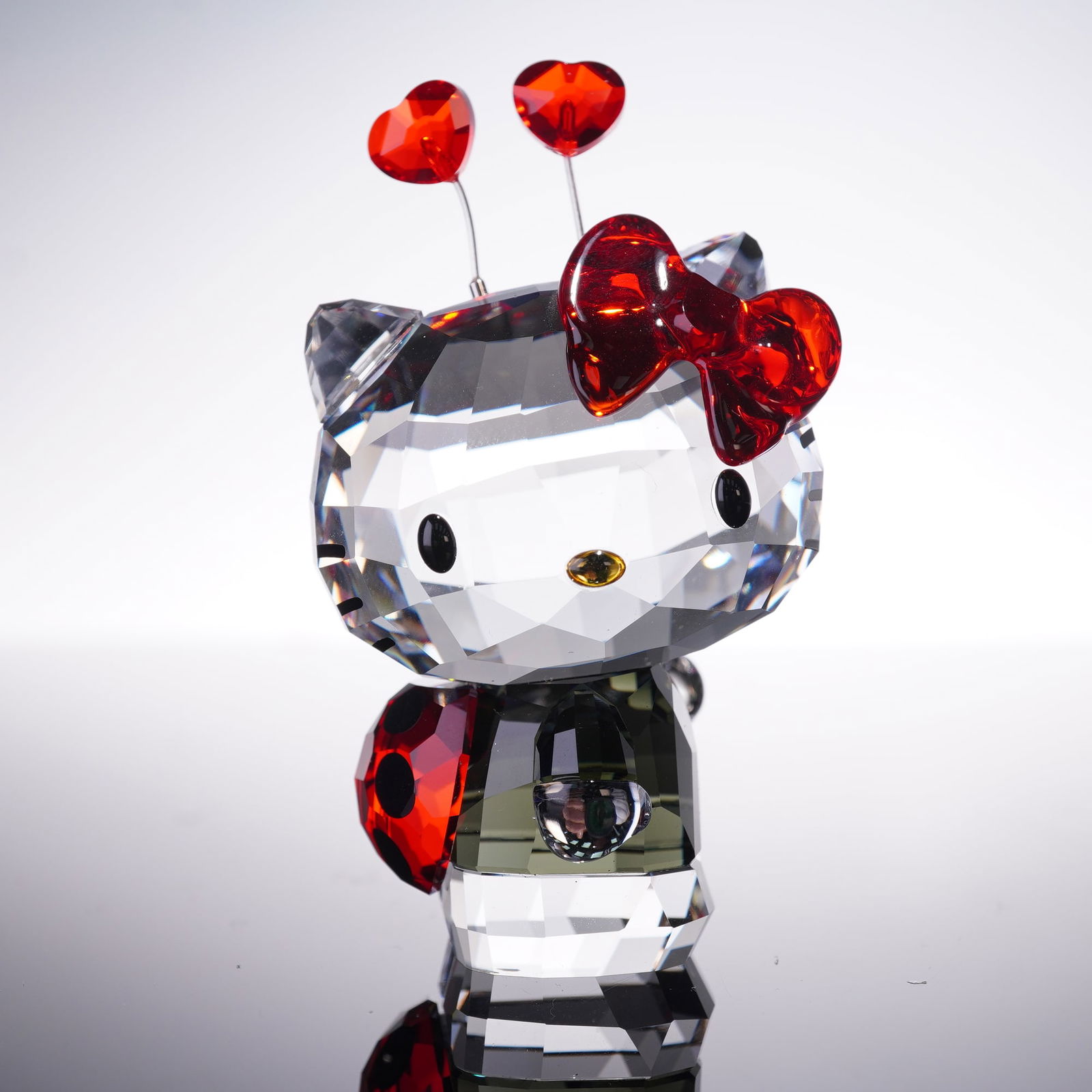 Swarovski Crystal Figurine, Lady Bug Hello Kitty: A delightful crystal figurine depicting Hello Kitty adorned in a whimsical ladybug attire. She sparkles in Black Diamond and clear crystal with printed black whiskers. Further embellished with radiant