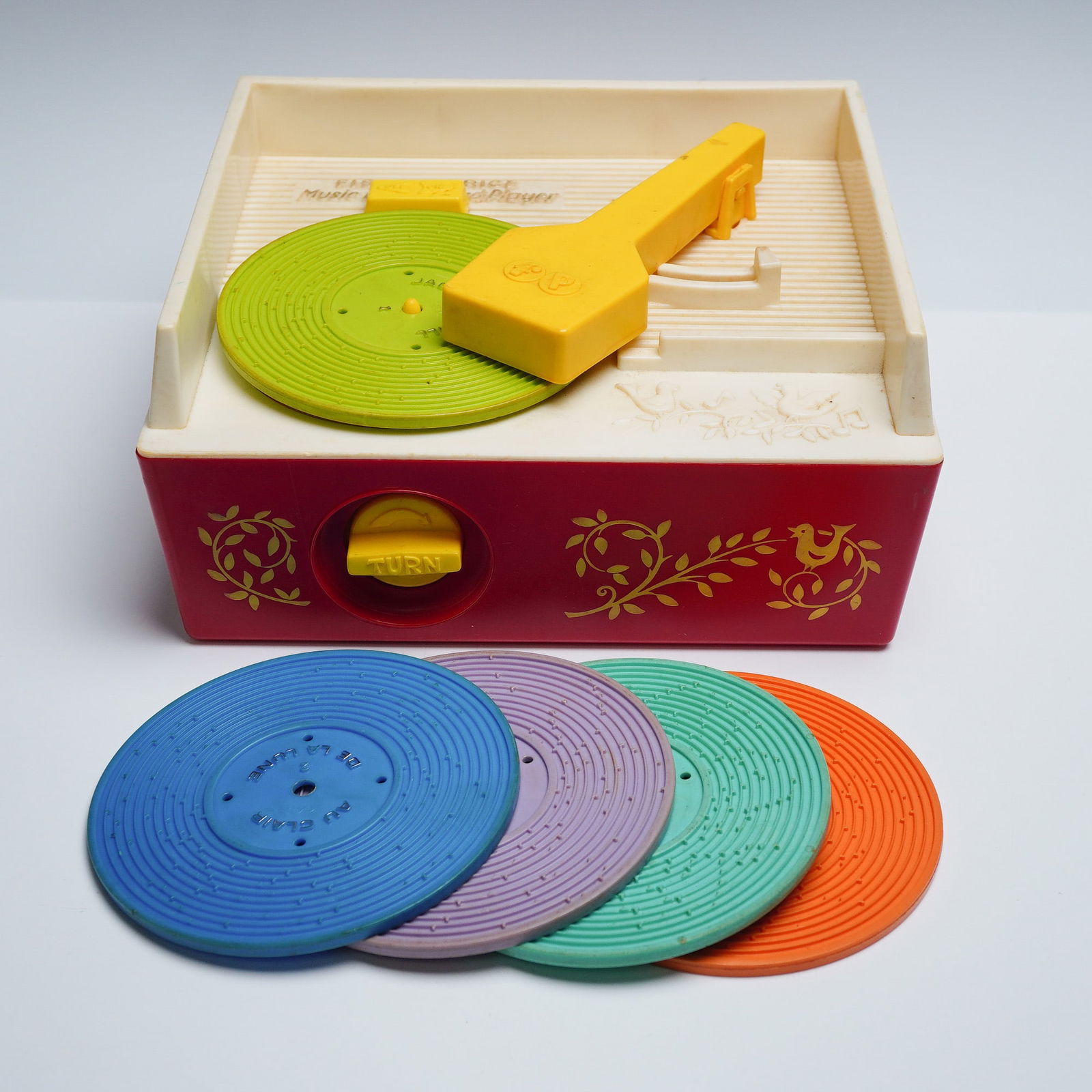 6pc Fisher Price Toy Record Player with Records: Vintage Fisher Price Music Box Record Player in red and cream plastic with yellow tonearm and handle, featuring charming floral and bird decals. Includes five colorful toy records in blue, purple, gre