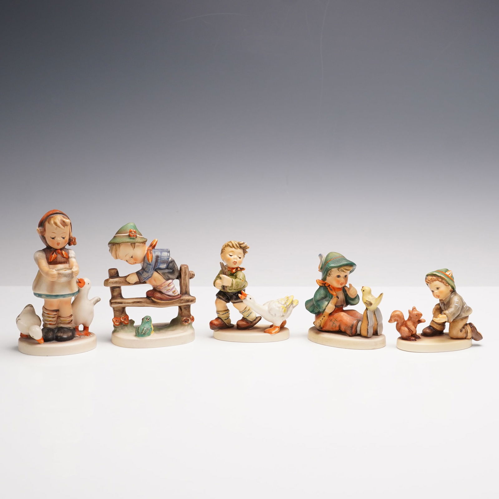 5pc Goebel Hummel Figurines Group, Animal Training: A delightful gathering of five Goebel Hummel figurines, each capturing a playful moment between children and their animal friends. This lot includes Singing Lesson 63, where a young girl patiently sha