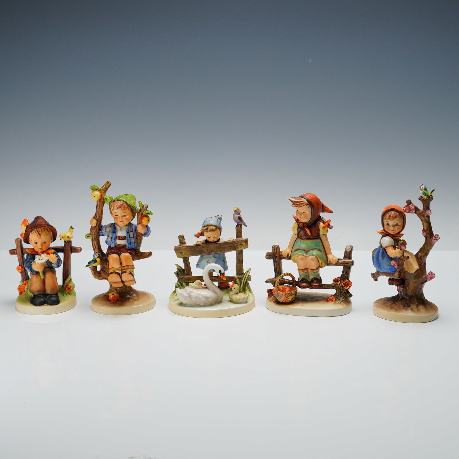 5pc Goebel Hummel Outdoor Themed Figurines: Charming set of five Goebel Hummels. Just Resting features a girl seated on a wooden fence with flowers at her side. Feathered Friends shows a young girl admiring a swan while a bird rests nearby. App