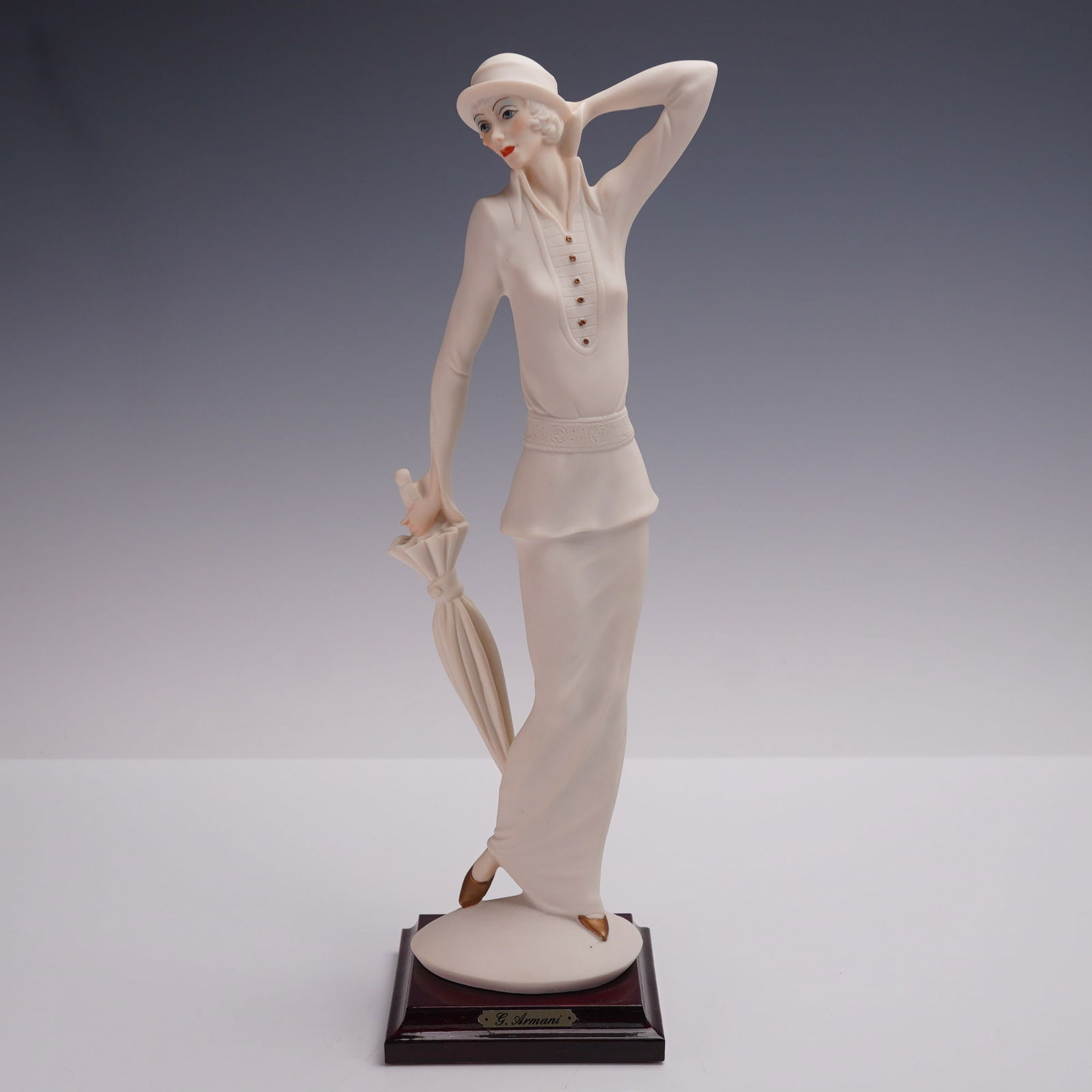 Florence Giuseppe Armani Figurine, Lady with Umbrella: A porcelain figurine depicting a lady in a long dress holding an umbrella. Features hand-painted details, embossed Capodimonte mark, and artist signature G. Armani on base. Mounted on a wooden base wi