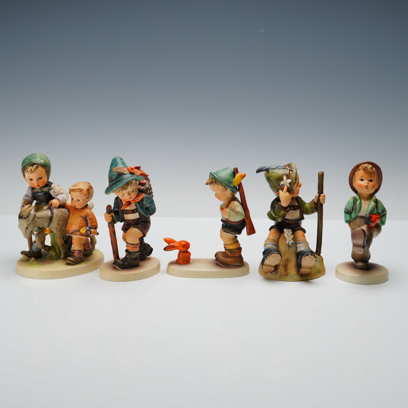 5pc Goebel Hummel Wilderness Travel Themed Figurines: This delightful lot features five Goebel Hummel figurines. Flower Vendor shows a boy with a walking stick and a large basket of flowers on his back. The Mountaineer depicts a confident boy seated on a