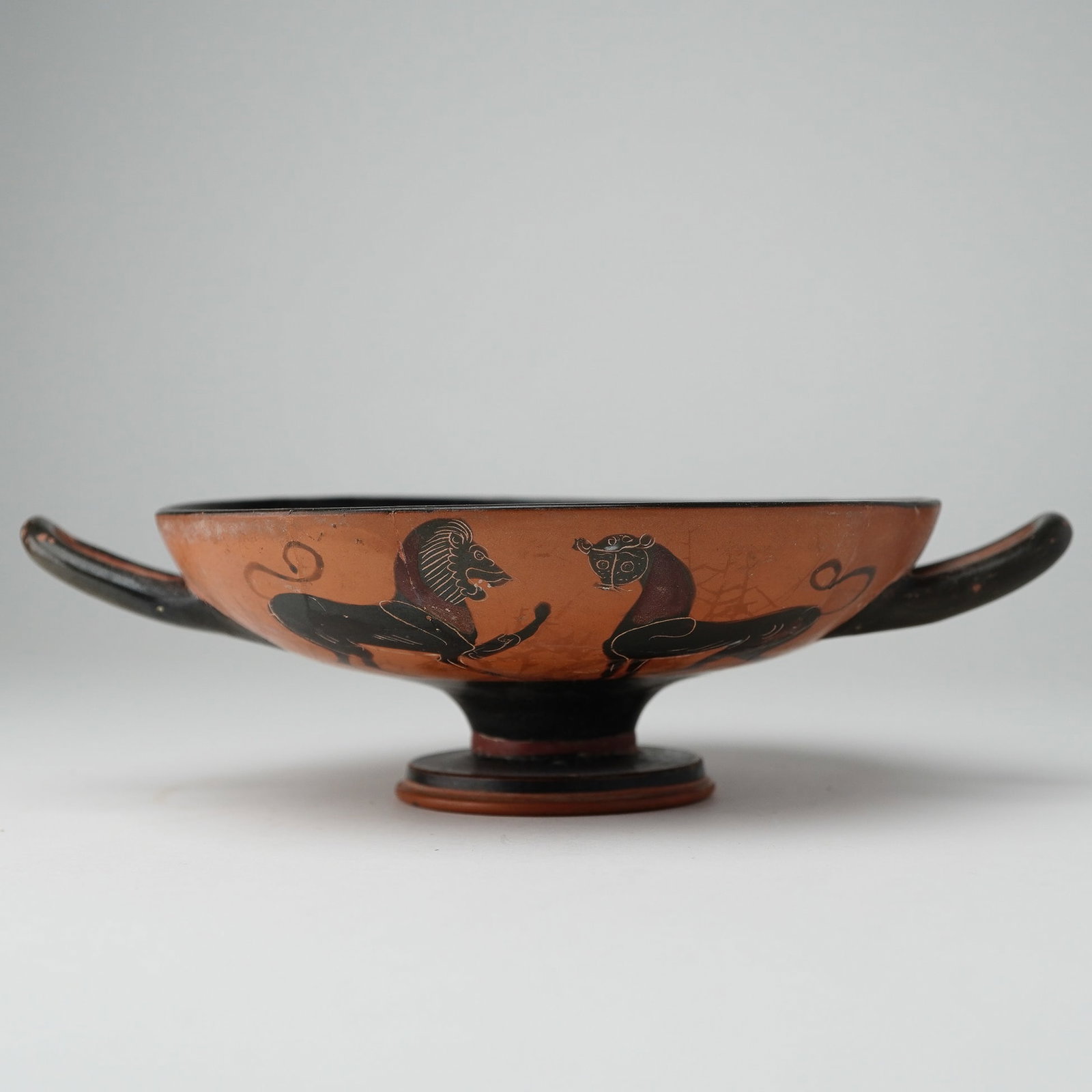 Ancient Greek Attic Black-Figure Kylix, 6th Century BCE: This ancient Greek Attic black-figure kylix dates to the 6th century BCE and served as a wine cup used during symposia, or after-dinner drinking parties. The kylix features a wide, shallow bowl with t
