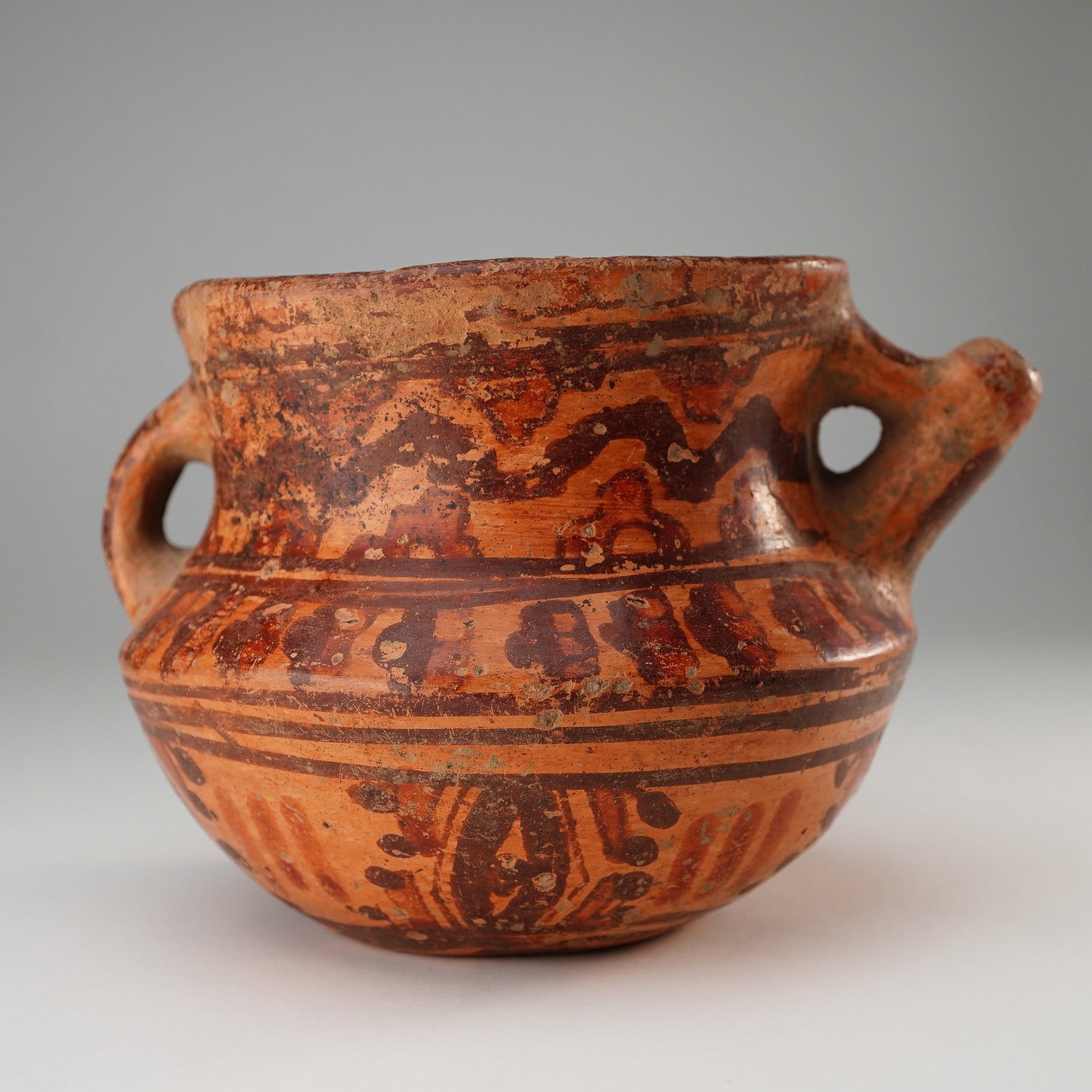 Pre-Columbian Double-Handle Painted Vessel: This double-handle painted vessel is crafted from reddish clay and features a globular body with a slightly flared rim. The vessel is adorned with polychrome painted decoration, including linear and g