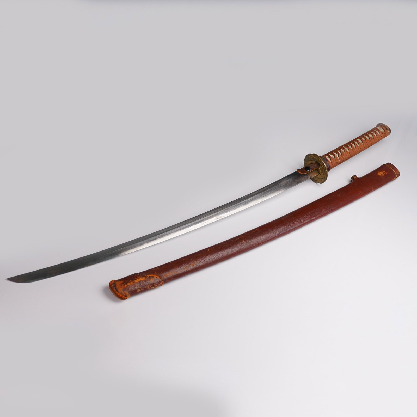 Japanese Military Ceremonial Katana Sword: This Japanese military ceremonial katana sword features a traditionally wrapped tsuka handle in brown cloth over possibly rayskin (samegawa), showcasing a tight and intricate pattern. The kashira (pom