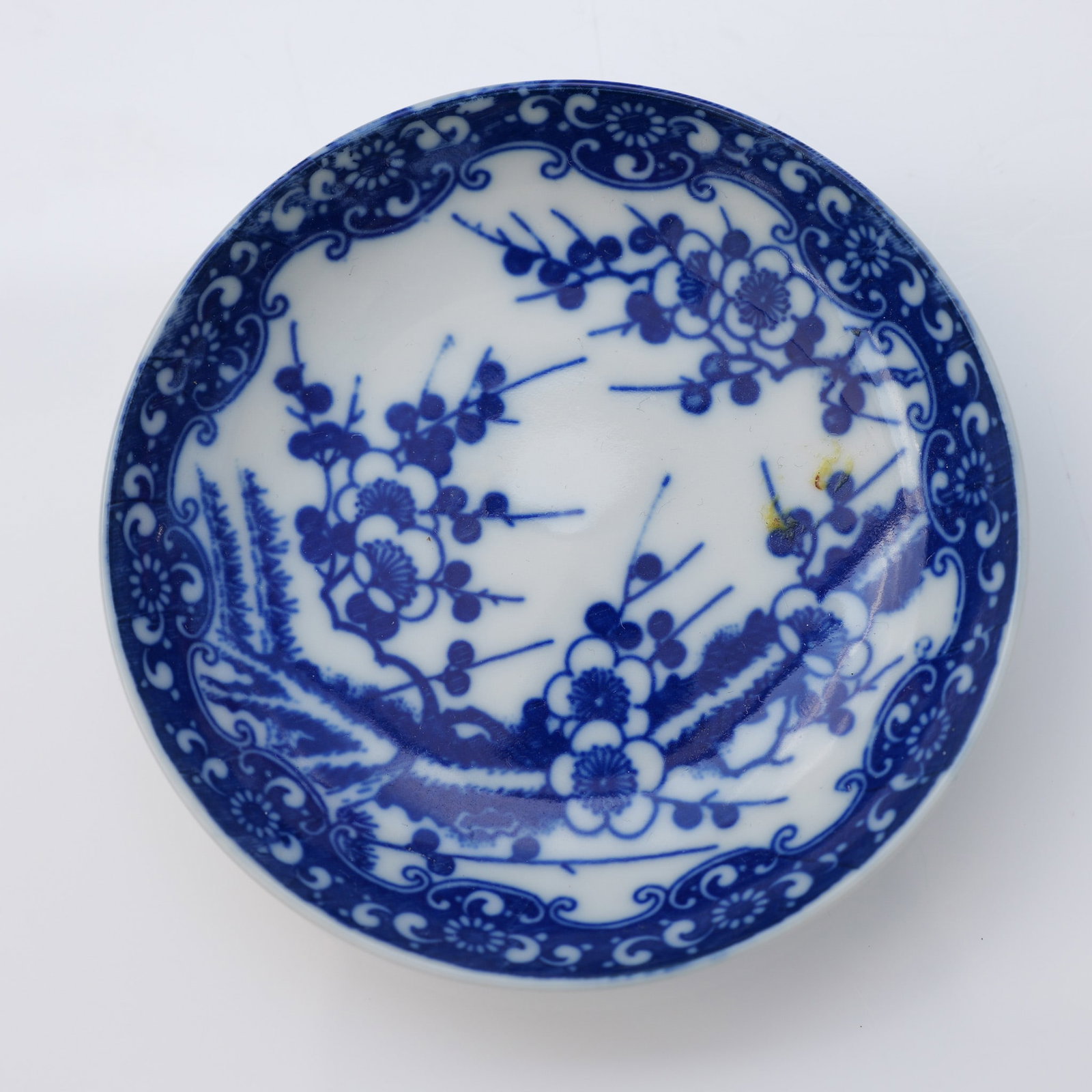 Japanese Porcelain Sakura Blossom Saucer: Japanese porcelain saucer featuring a blue and white underglaze floral motif. The central design consists of sakura (cherry blossom) branches with clustered plum blossoms rendered in deep cobalt blue,