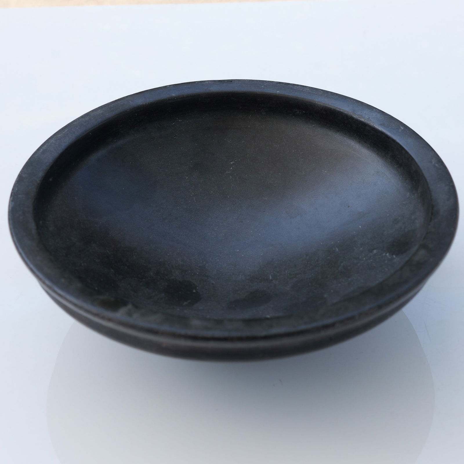 Asian Black Glazed Pottery Bowl: Black pottery bowl featuring a satin finish across the interior and exterior surfaces. The shallow, wide form sits on a slightly raised circular foot with a recessed base. The bowl is finished in a de