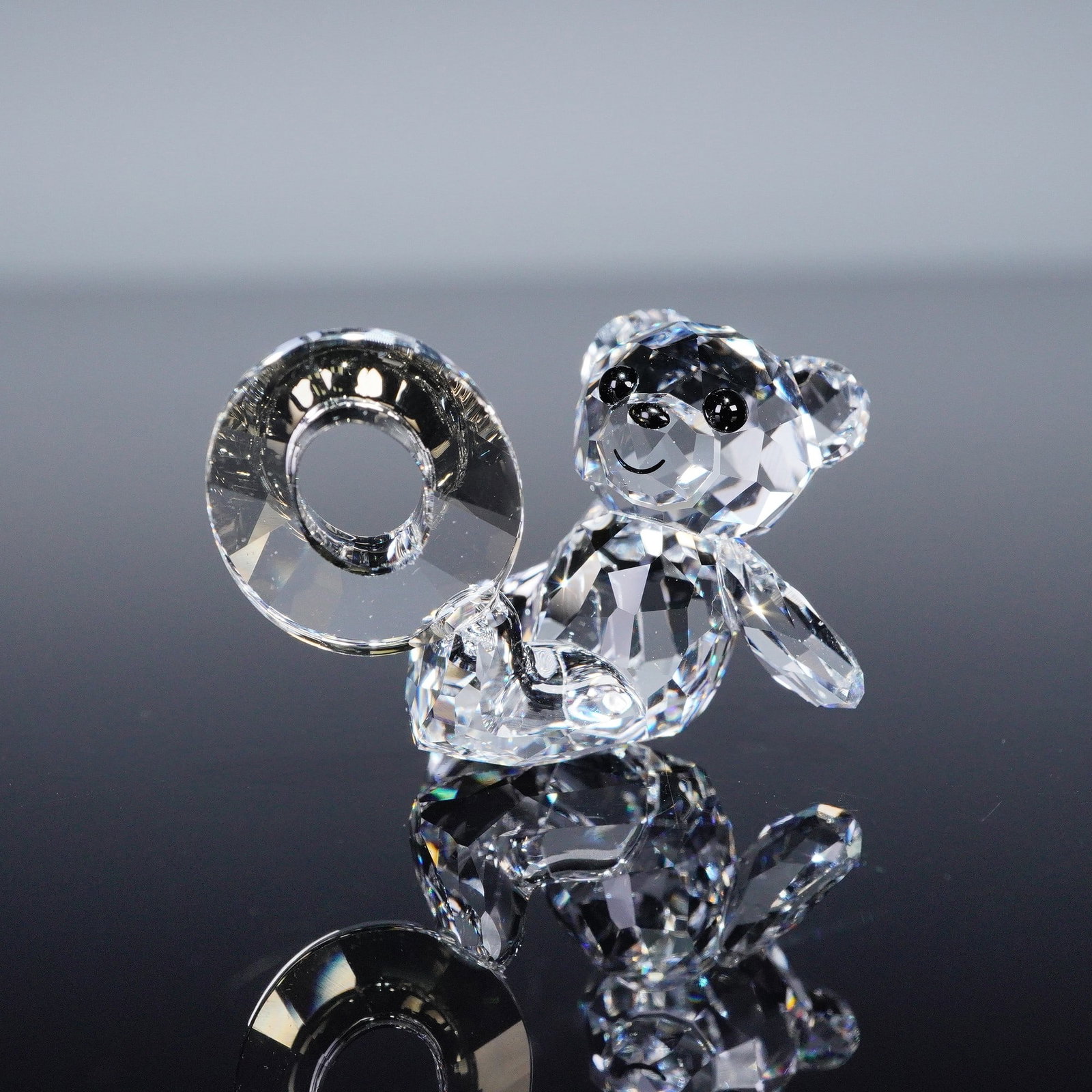 Swarovski Lovlots Crystal Kris Bear Figurine, Number Zero: This clear crystal figurine depicts the Kris Bear holding a clear crystal number "0." The bear features faceted detailing with black crystal eyes and nose. The underside is etched with the Swarovski s