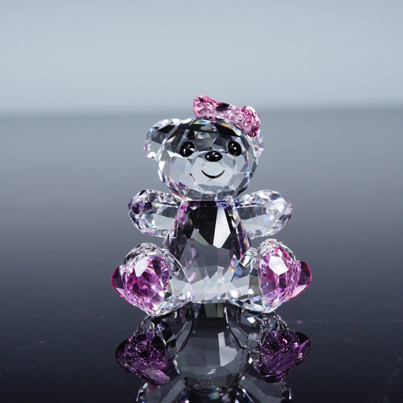 Swarovski Lovlots Crystal Kris Bear Figurine, Sweetheart: Crafted in clear faceted crystal with pink crystal bow and pink crystal heart-shaped footpads, arms extended in front. Underside bears the Swarovski swan mark. Figurine is accompanied by the original 