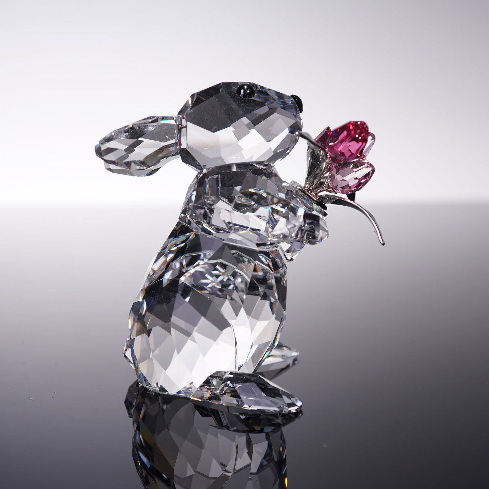 Swarovski Crystal Figurine Rabbit with Tulips 5004634: Swarovski crystal figurine Rabbit with Tulips, designed by Heinz Tabertshofer. The rabbit is crafted in clear faceted crystal with Jet crystal eyes and holds a bouquet of tulips in Indian Pink and Lig