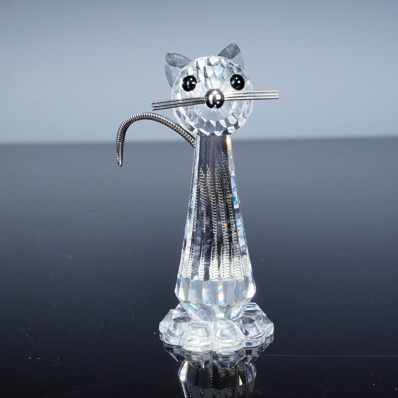 Swarovski Crystal Figurine, Cat: A Swarovski Silver Crystal figurine depicting a stylized cat with faceted crystal body, black crystal eyes, metal whiskers, and curled metal tail. The piece is marked with the Swarovski swan backstamp