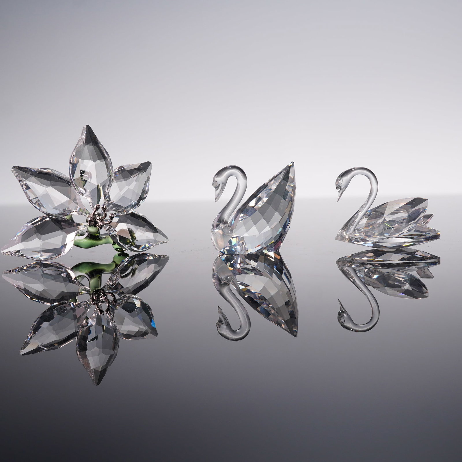 3pc Swarovski Crystal Figurines, Orchid and Swans: A refined trio of Swarovski crystal figurines consisting of an Orchid and two Swans. Each is hallmarked with the Swarovski swan logo and accompanied by its original box. One of the swans is the Centen