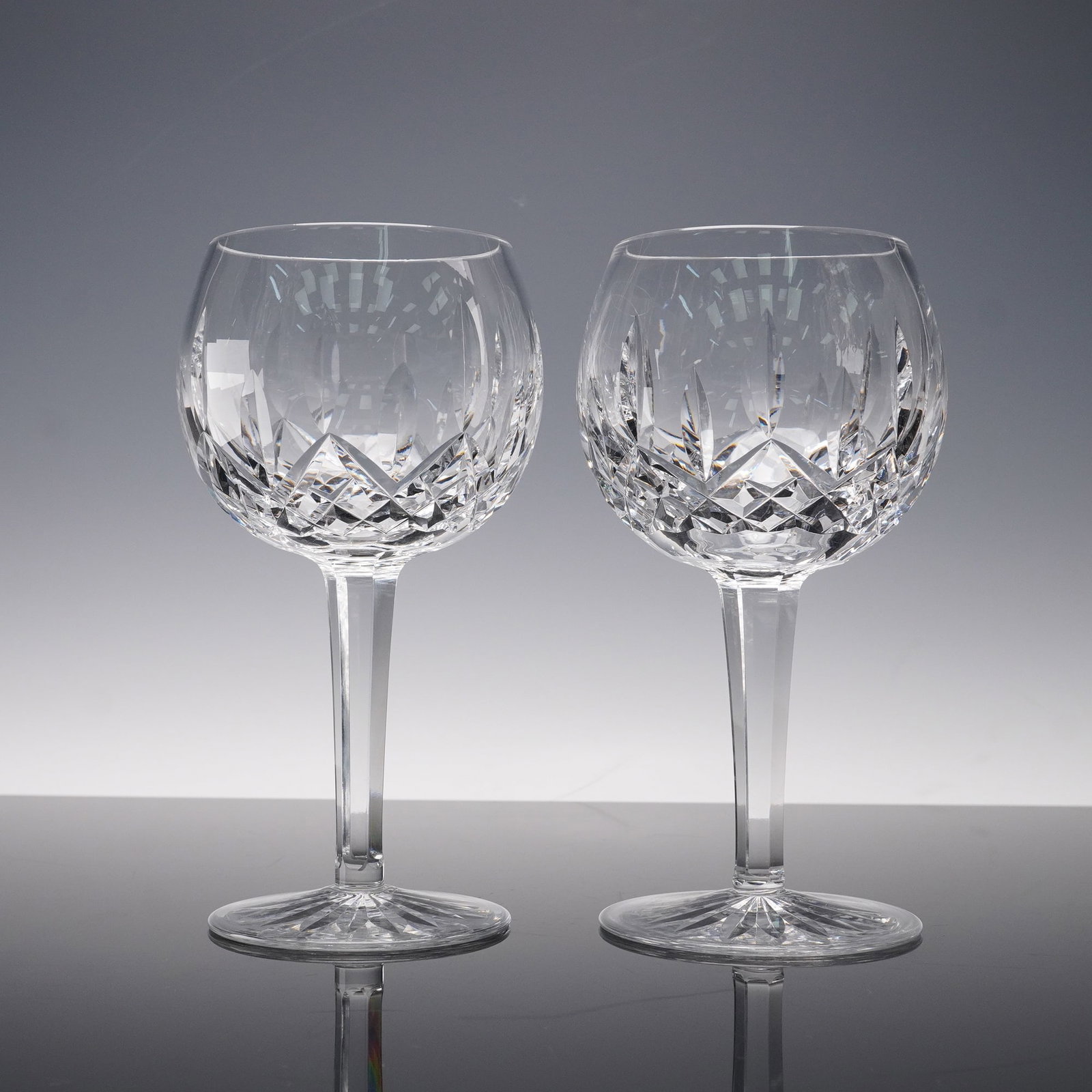 Pair of Waterford Crystal Wine Glasses, Lismore: air of Waterford Crystal oversized wine glasses in the Lismore pattern showcasing brilliant wedge and diamond cuts that shimmer with every angle of light. Each piece rests on a tall faceted stem and a