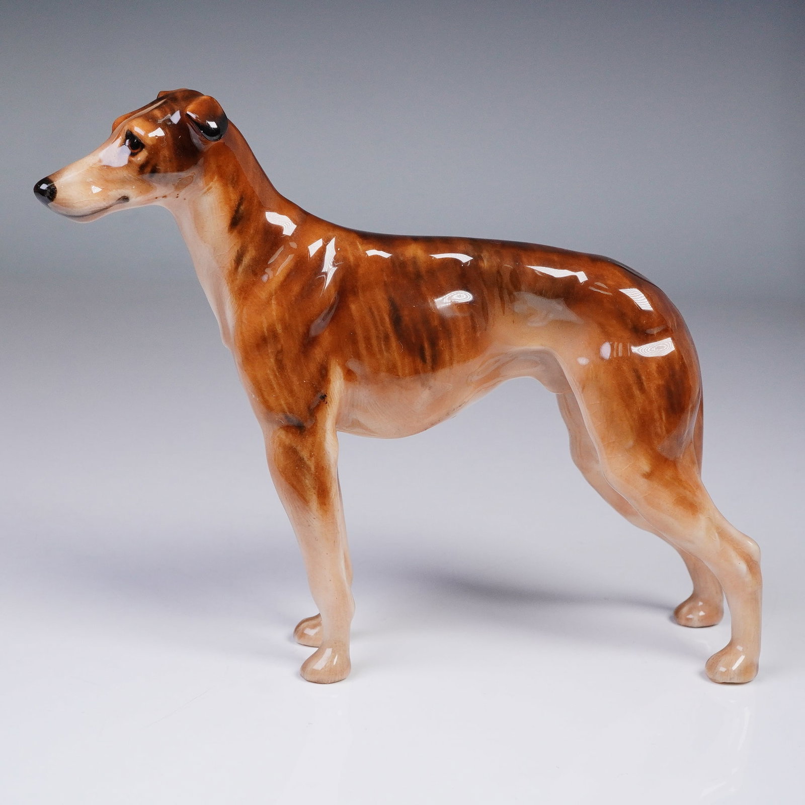 Royal Doulton Figurine, Greyhound HN1067: A finely modeled Royal Doulton figurine, HN1067, depicting a standing greyhound in a graceful pose. Crafted in bone china and hand-painted in shades of warm brown with natural markings, the piece refl