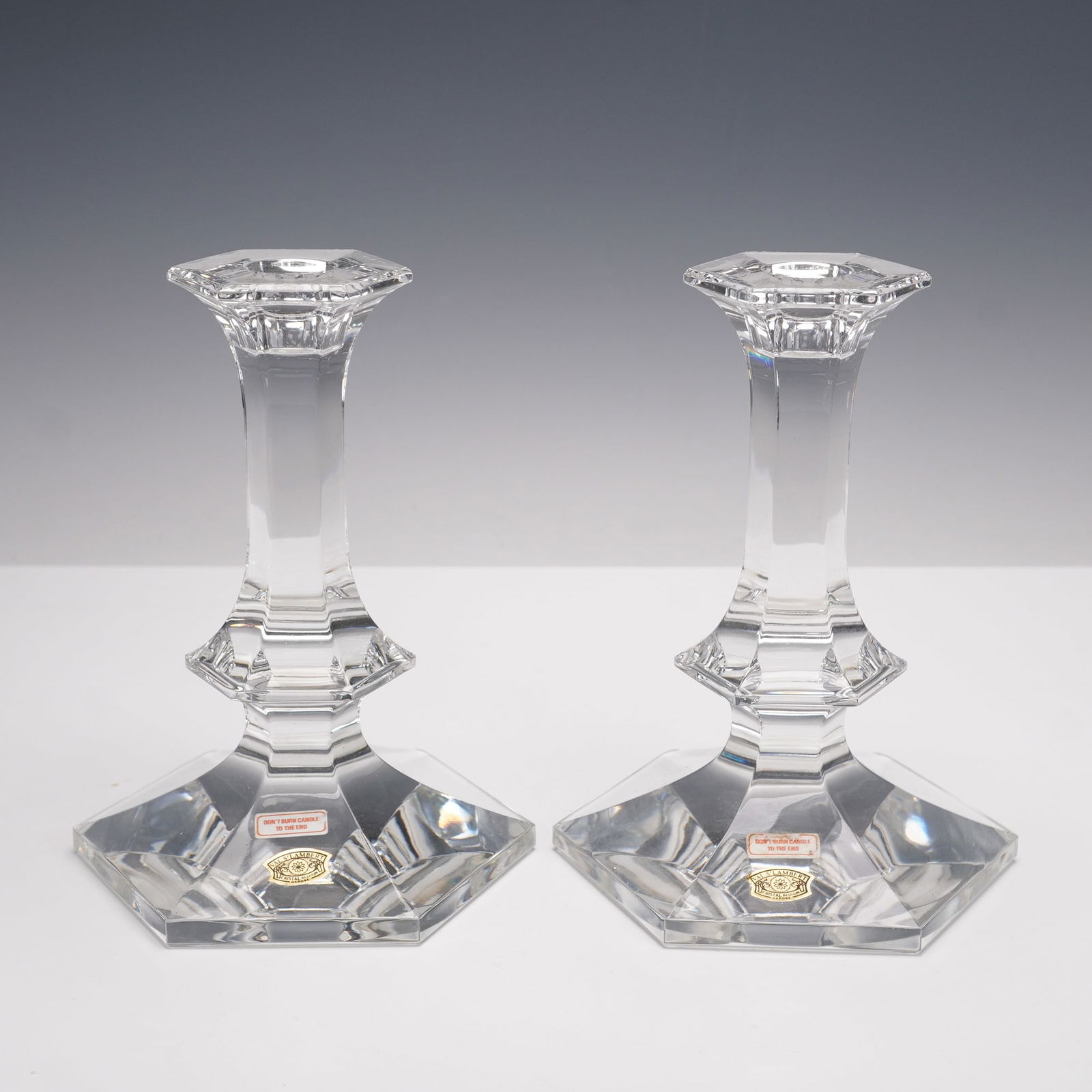 Pair of Val St Lambert Crystal Elysee Candlesticks: Pair of Val St Lambert crystal candlesticks in the Elysee pattern, featuring faceted hexagonal bases, tapering stems, and flared candle cups. Each retain original Val St Lambert foil labels and are et