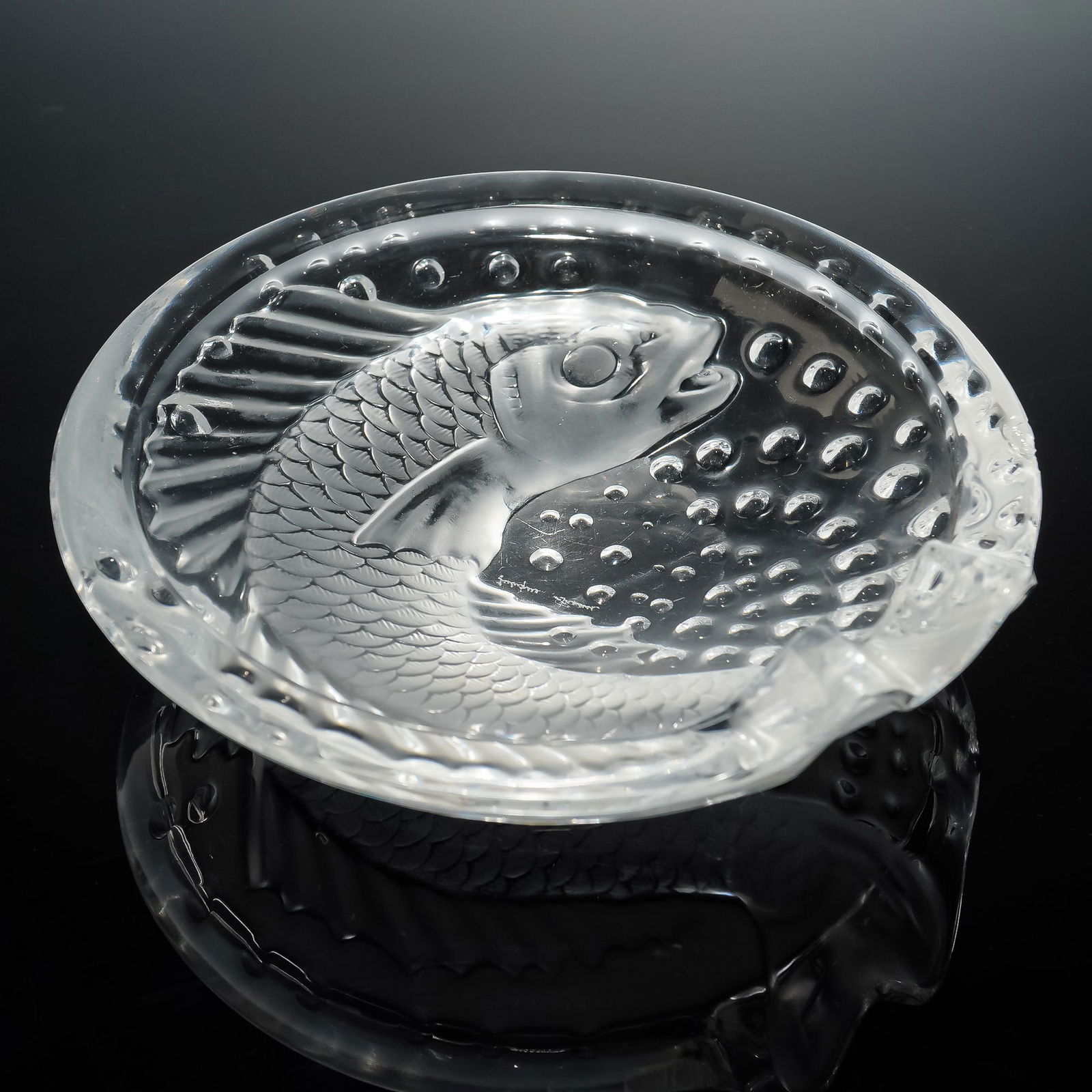 Lalique France Crystal Ashtray, Concarneau: A Lalique France Concarneau crystal ashtray featuring a relief molded fish design surrounded by bubble motifs, executed in frosted and clear finish. Signed Lalique France to the base. Issued: 20th cen