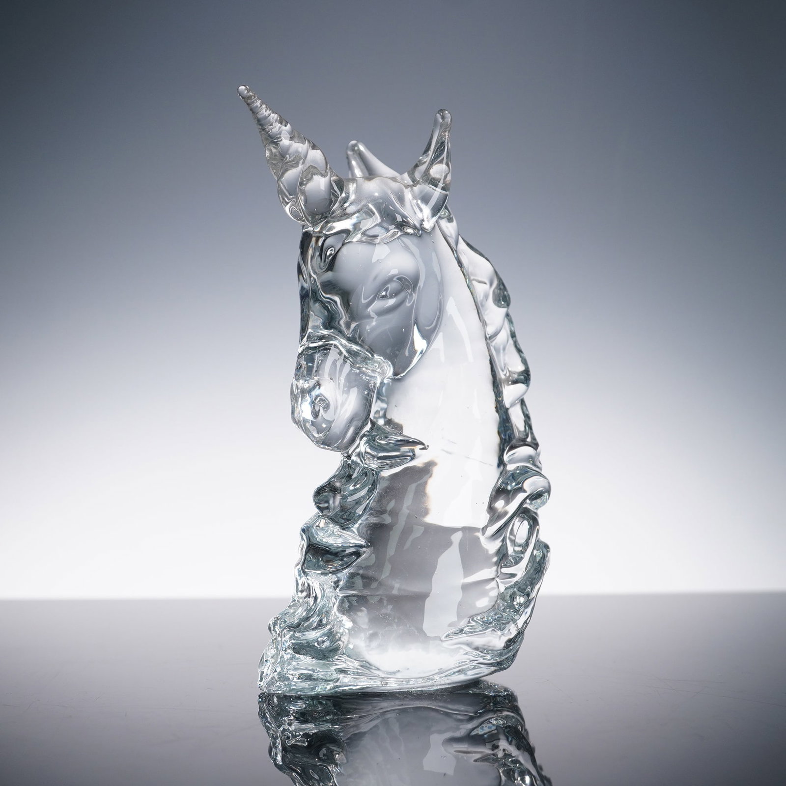 Art Glass Paperweight, Unicorn: Clear art glass paperweight modeled as a unicorn head with spiral horn, flowing mane, and polished flat base, likely late 20th century studio production, crisp optical clarity with occasional tiny bub