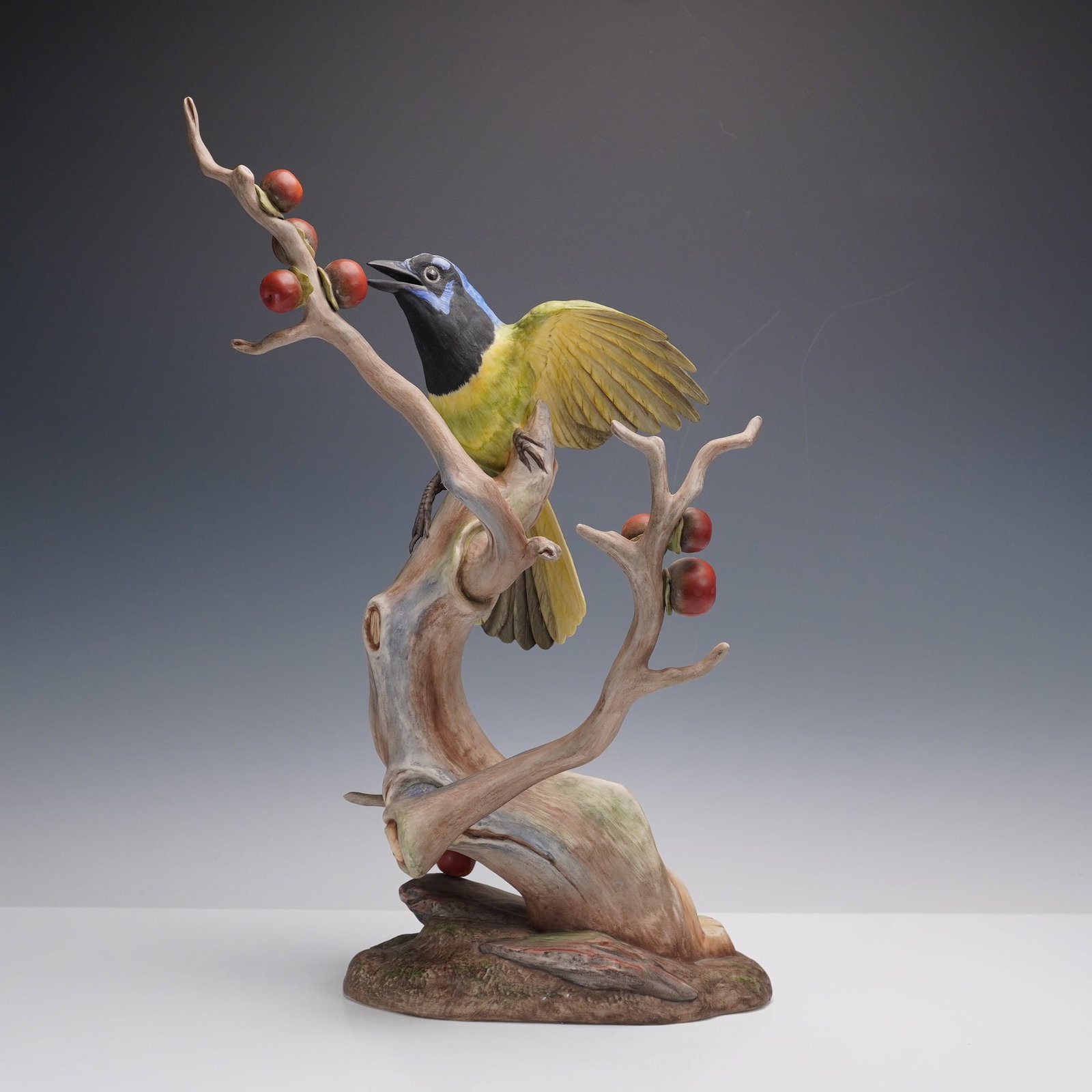 Boehm Porcelain Figurine, Green Jayes 486I: Exquisite limited edition figure depicting a green jay perched upon a gnarled tree branch adorned with clusters of red fruit. The bird is rendered with finely detailed plumage in vibrant shades of gre