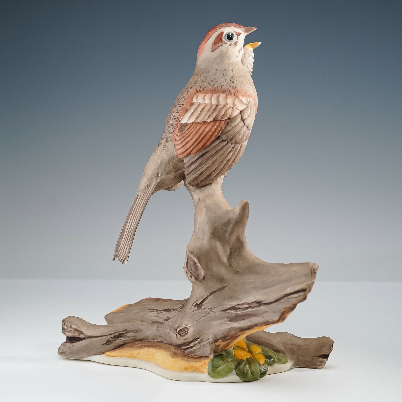 Boehm Porcelain Figurine, Tree Sparrow 468: A finely crafted Boehm porcelain figurine depicting a tree sparrow perched on a weathered branch with small yellow blossoms at the base. The bird is rendered with soft hand painted detail in brown, ru