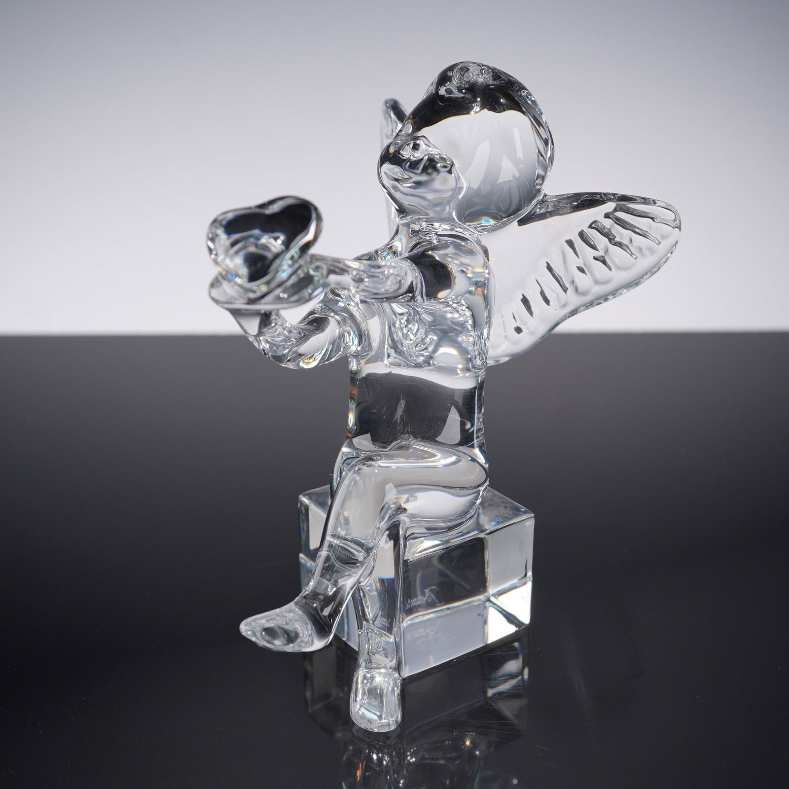 Baccarat Crystal Figurine, Cupid: A Baccarat crystal figurine depicting Cupid, seated on a cube pedestal with wings spread and holding a heart. Finely crafted in clear crystal, showcasing Baccarat's renowned artistry and precision. Th