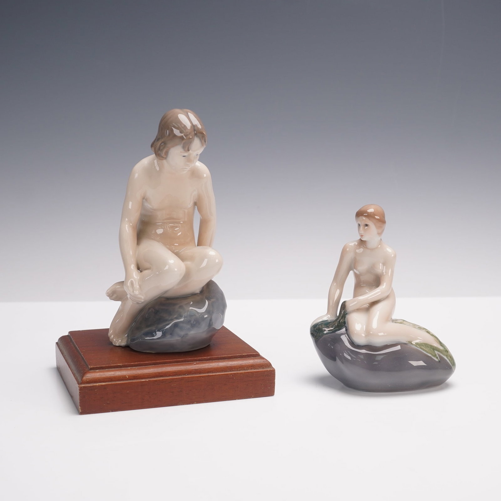 2pc Royal Copenhagen Porcelain Figurines, Girl on Stone & Little Mermaid: A pair of Royal Copenhagen porcelain figurines depicting young maidens seated on rocks. The first, model 1254, portrays a girl with short hair seated thoughtfully on a stone. The second, model 1009, r