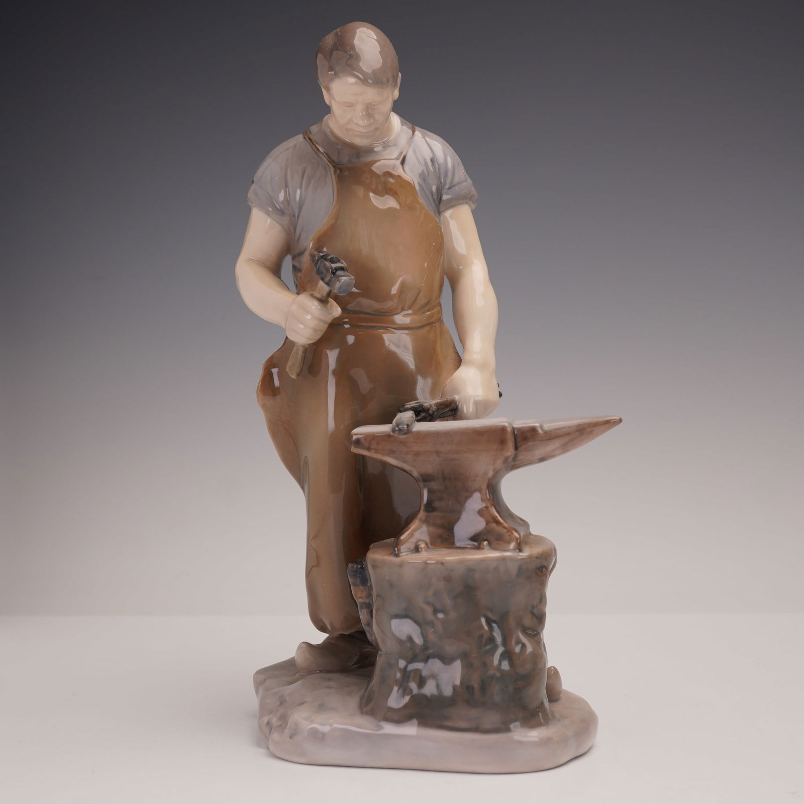 Bing & Grondahl Porcelain Figurine, Blacksmith, 2225: A finely modeled Bing & Grondahl porcelain figurine, #2225, titled The Blacksmith, designed by Danish sculptor Axel Locher (1879–1941). This striking piece depicts a muscular craftsman standing at h
