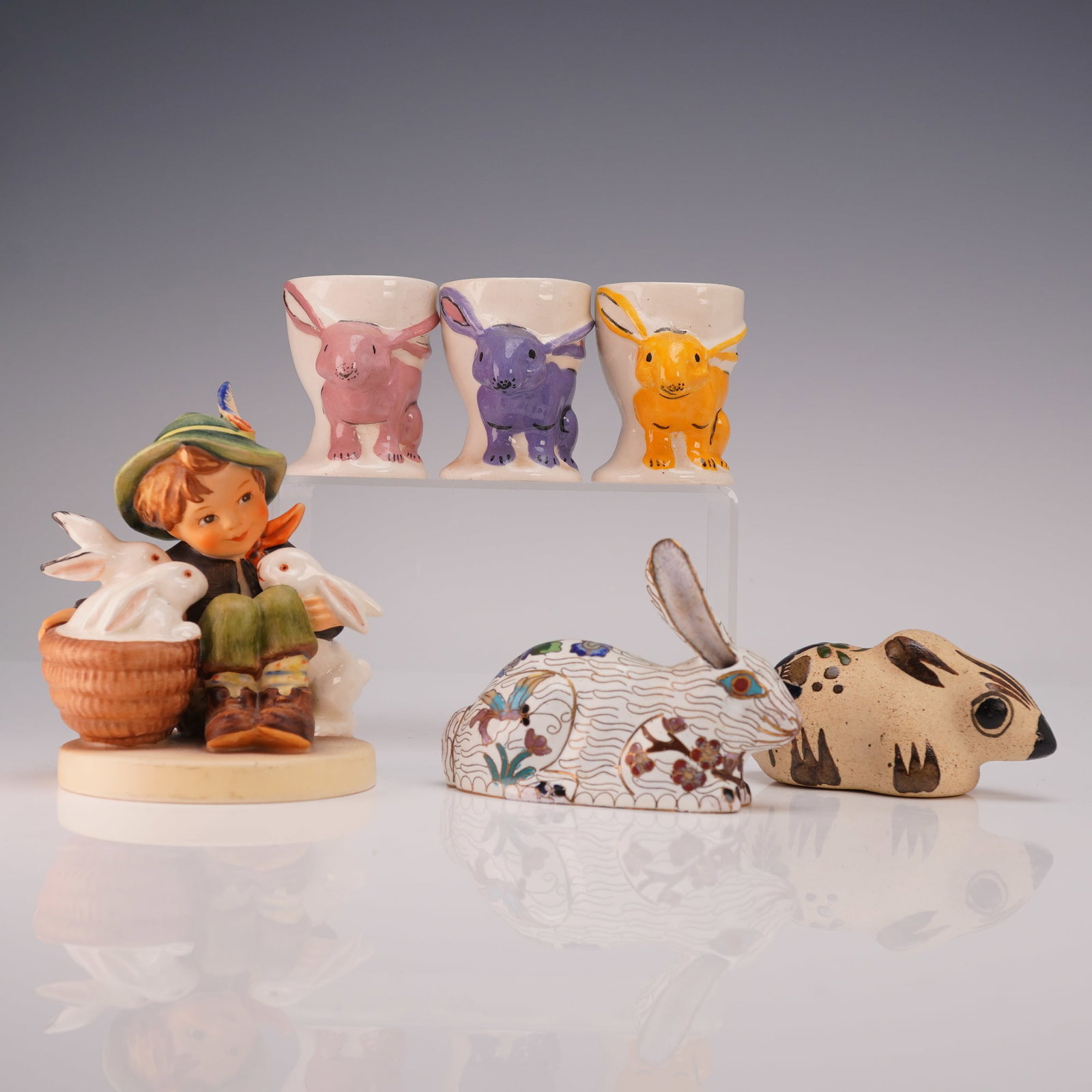 6pc Collection of Rabbit Figurines and Hummel Figure with Rabbit: Includes 3 handmade and hand painted ceramic rabbit egg cups in pink, purple, and yellow, each marked to base, together with a cloisonne rabbit decorated with floral motifs, a Mexican pottery rabbit f