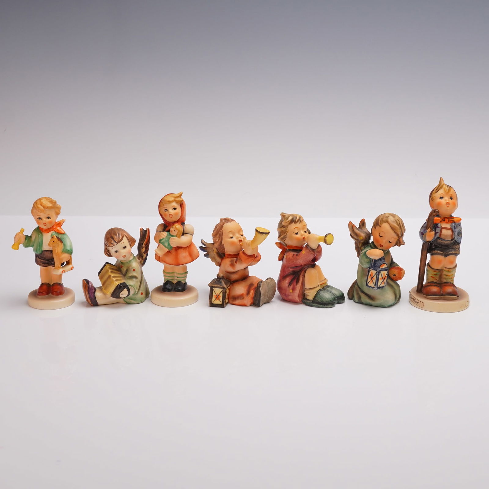 7pc Goebel Hummel Childhood Figurines: 7-piece collection of porcelain figurines depicting charming childhood and angelic themes. Includes Boy with Horse (239), Angel with Accordion (11/39/1), Girl with Doll (239/B), Angel with Horn (359),