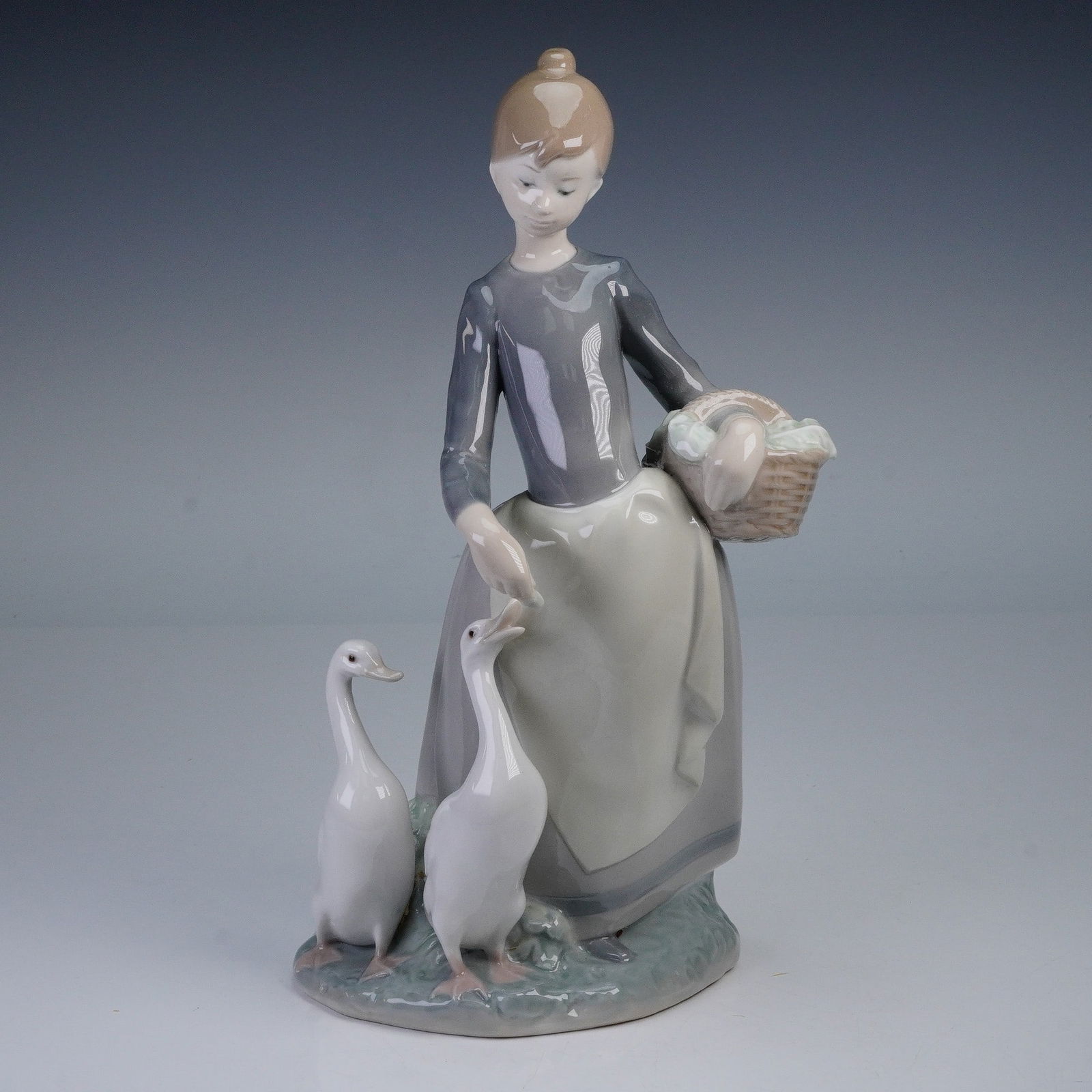 Lladro Porcelain Figurine, On the Farm 01001306: This charming Lladro figurine, titled On the Farm, depicts a young woman feeding two geese while holding a basket. Sculpted by Fulgencio Garcia, this beautifully detailed piece features delicate model