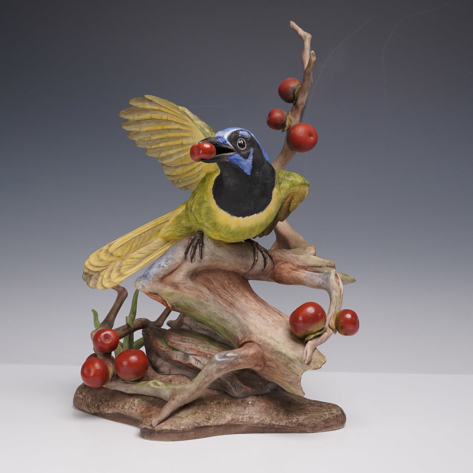 Boehm Porcelain Figurine, Green Jayes 486: Limited edition. The sculpture depicts a green jay perched on a naturalistic tree branch with clusters of red berries, one of which the bird holds in its beak. The bird is finished in shades of yellow