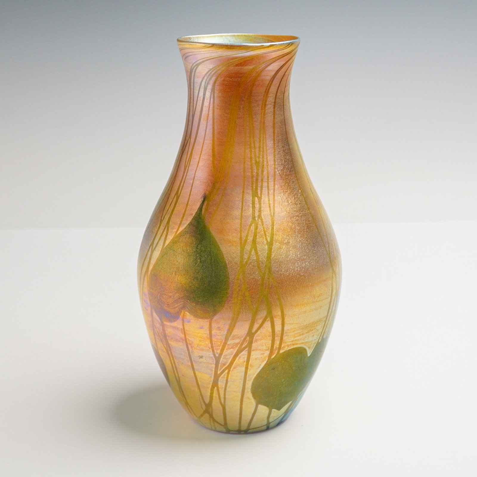 Louis Comfort Tiffany Favrile Glass Iridescent Leaf and Vine Vase: Featuring a baluster form vase with a narrow flaring rim, decorated with green heart-shaped leaves and trailing vine motifs extending vertically across the body. The surface exhibits a gold iridescent