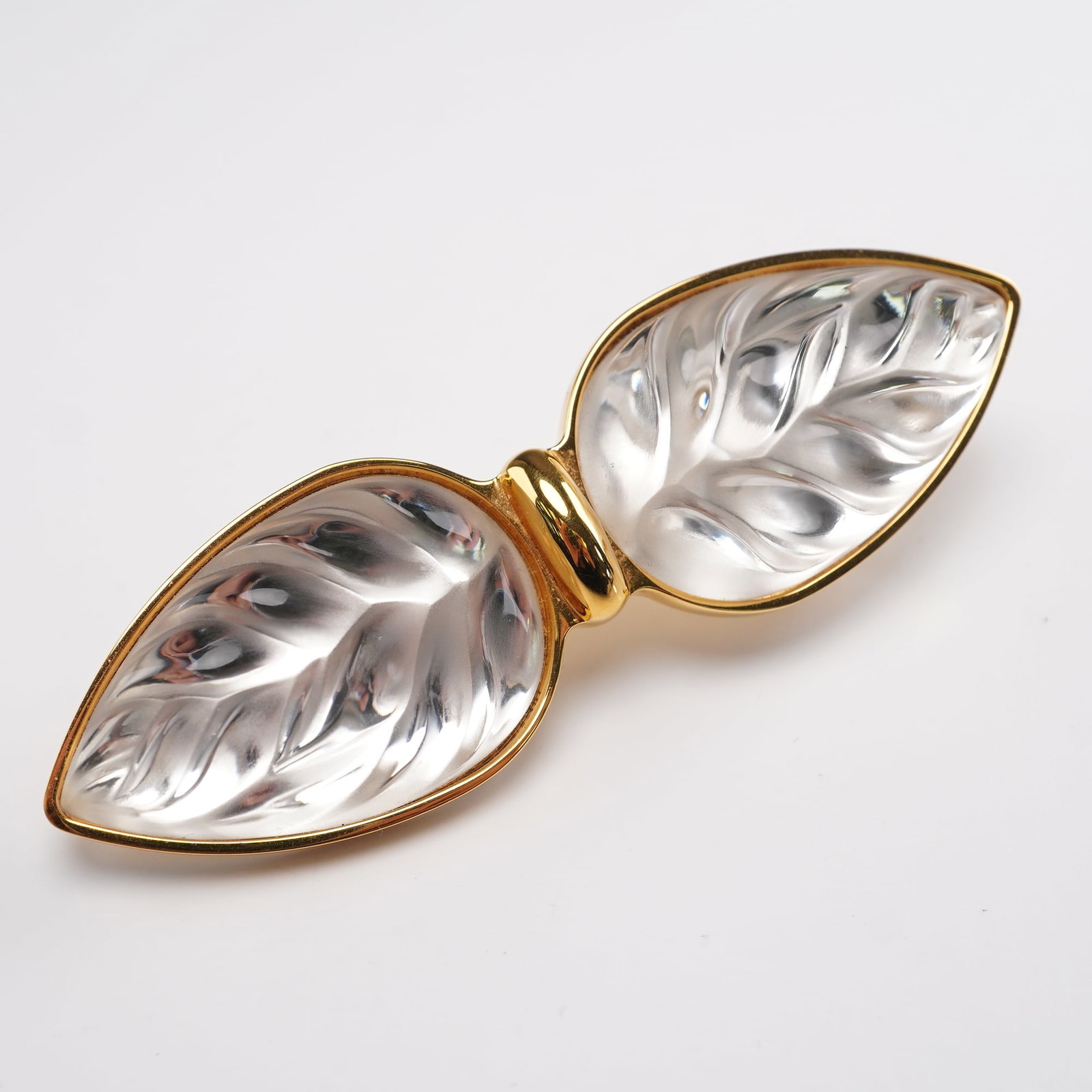 Lalique Clear Crystal Heliconia Belt Buckle: Elegant Lalique belt buckle featuring a twin leaf Heliconia motif crafted in clear crystal with frosted and polished detailing, framed in gold-tone metal. The sculpted crystal leaves display intricate