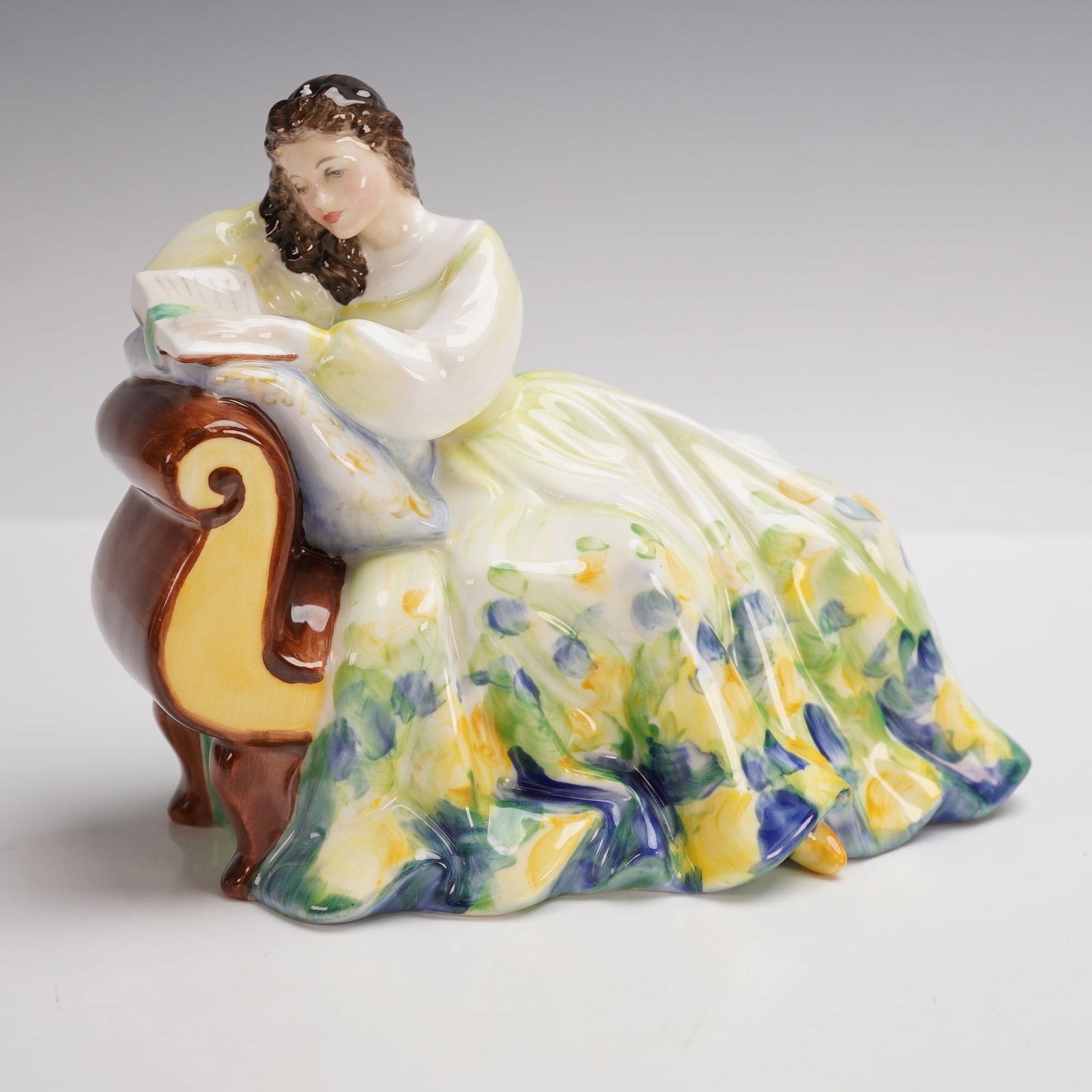 Royal Doulton Figurine, Solitude HN2810: The Solitude figurine from Royal Doulton captures a serene moment with a lady reclining on a chair, lost in her book. This fine china piece, modeled after the popular "Pretty Ladies" motif, features i