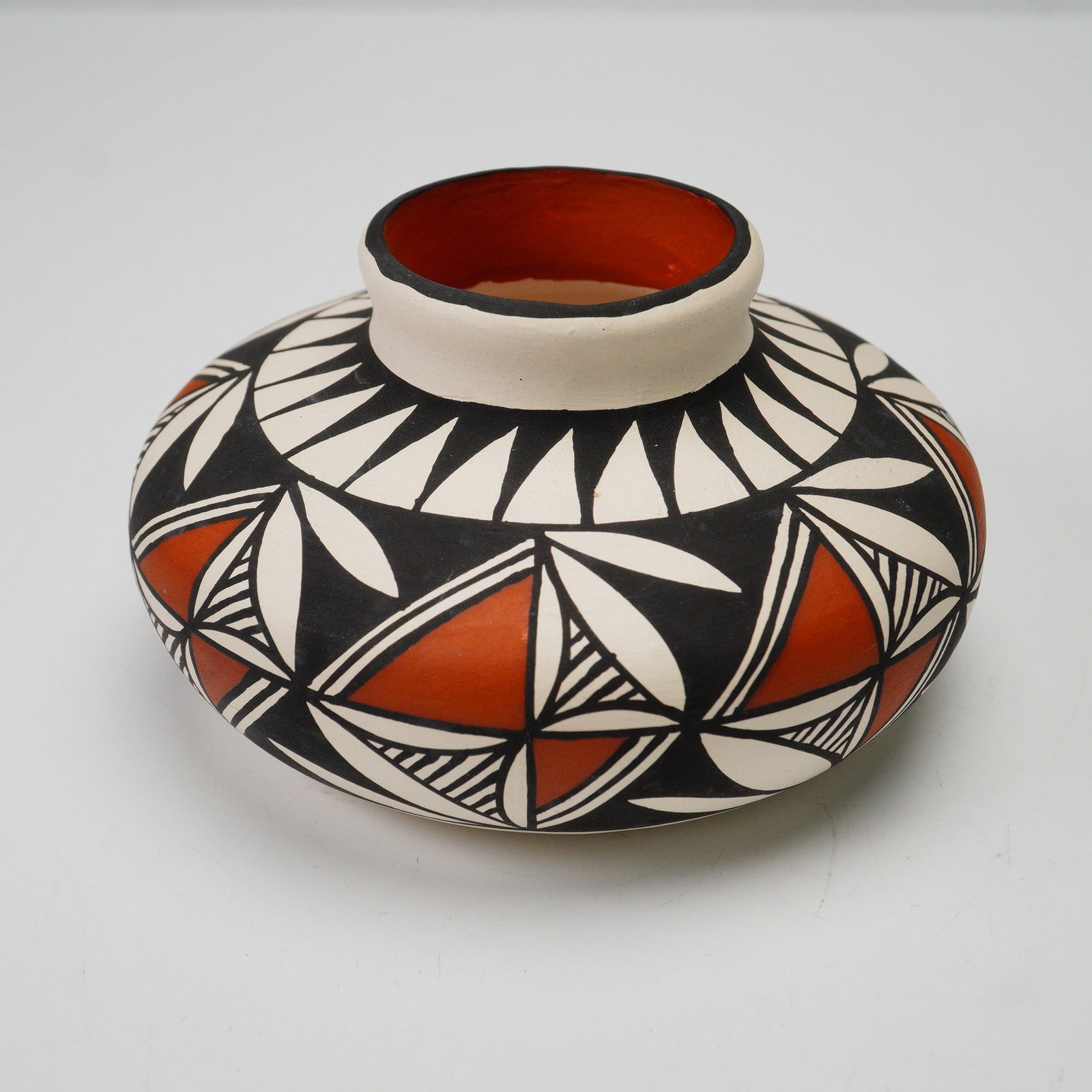 Gwen Patricio Acoma Pueblo Pottery Vase: This hand-painted pottery vase is signed by Gwen Patricio of Acoma Pueblo, New Mexico. The piece features a traditional red, black, and white palette with bold geometric and leaf-like designs encircli