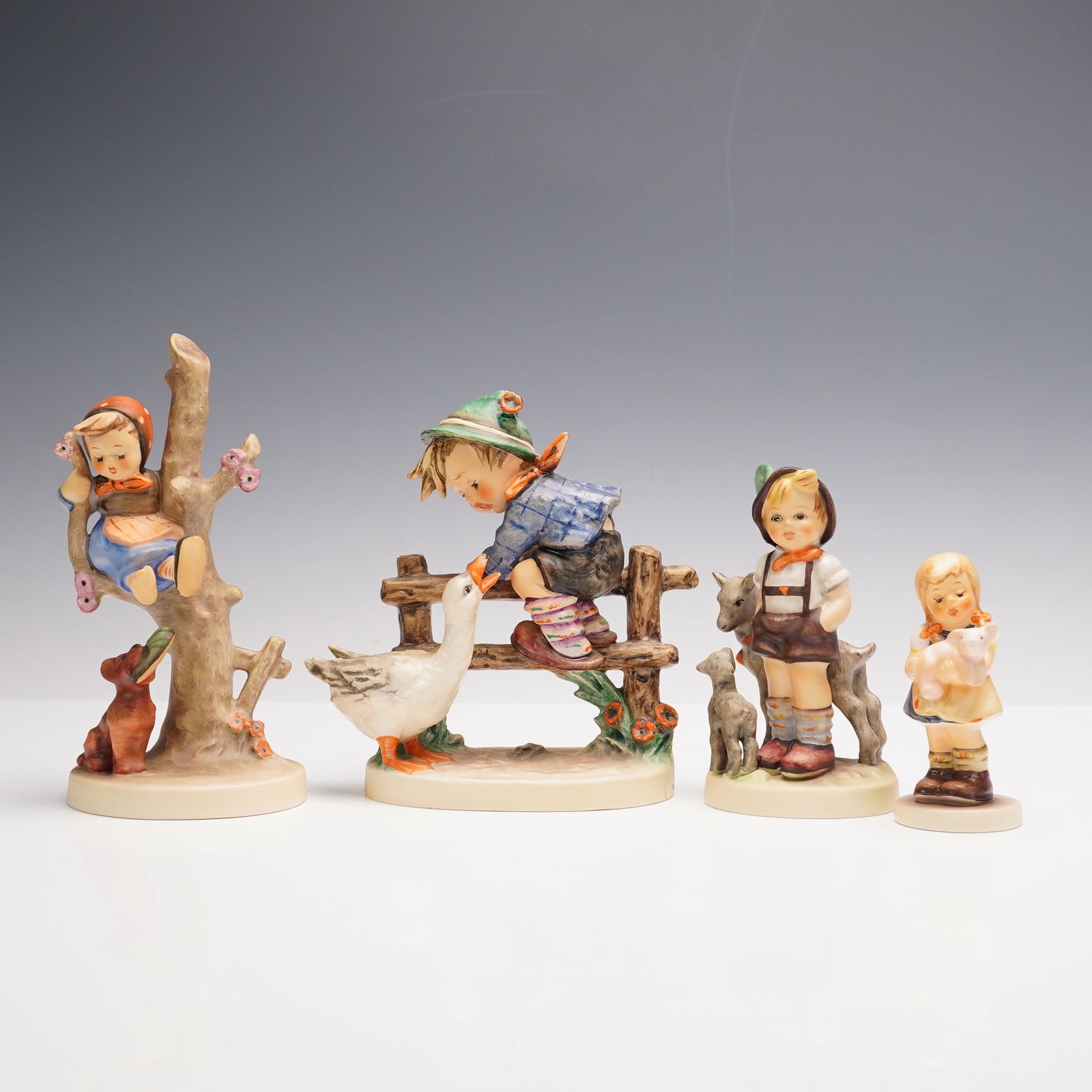 4pc Goebel Hummel Porcelain Figurines: A grouping of four porcelain figurines, each hand-painted with refined detail and imbued with rustic charm. Included are Out of Danger, Little Goat Herder, Pigtails, and Barnyard Hero. Modeled as chil