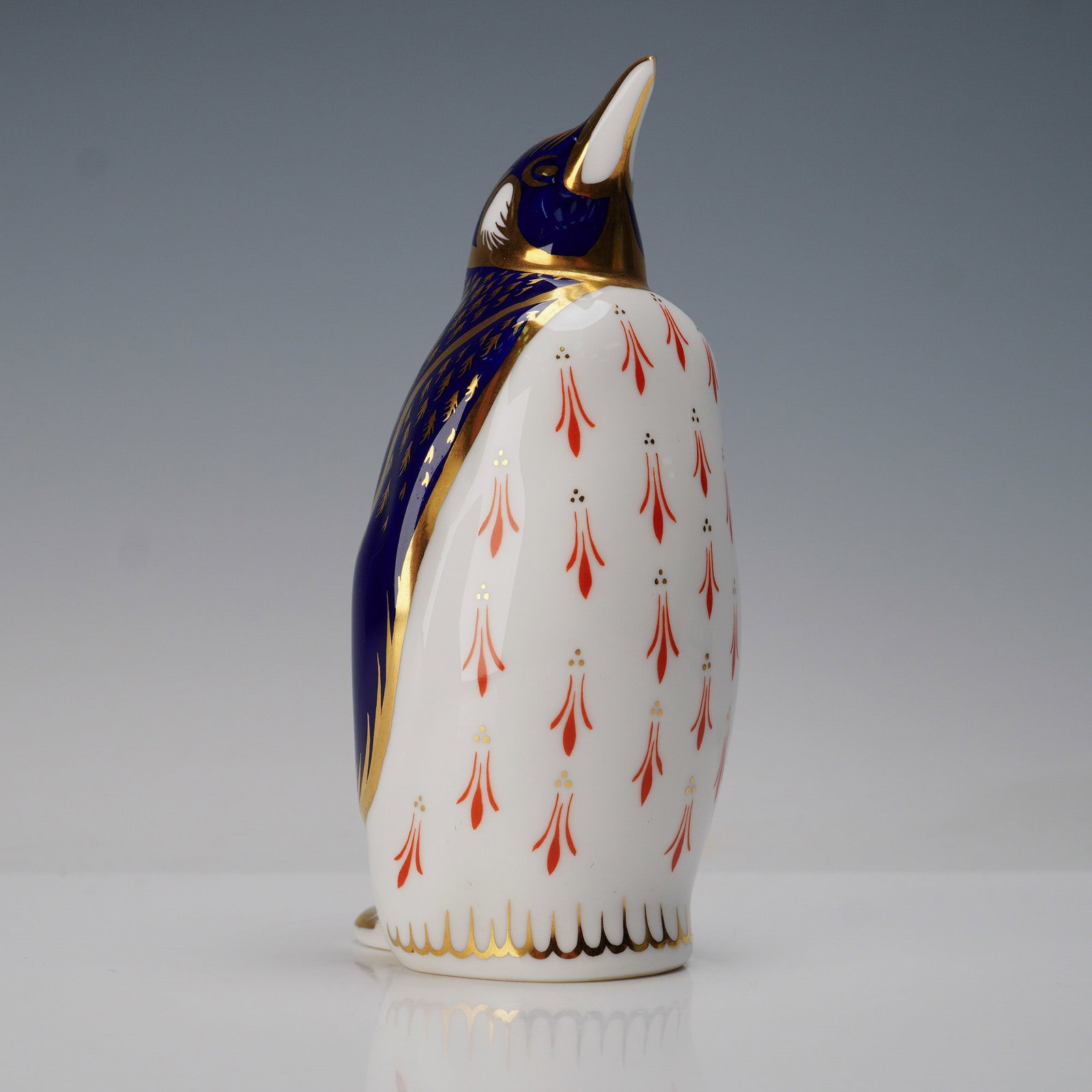 Royal Crown Derby Bone China Paperweight, Penguin: Decorated in the company's signature Imari-inspired palette. The figure features a rich cobalt blue back with intricate gilt feather detailing, contrasted by a white body adorned with repeating red an