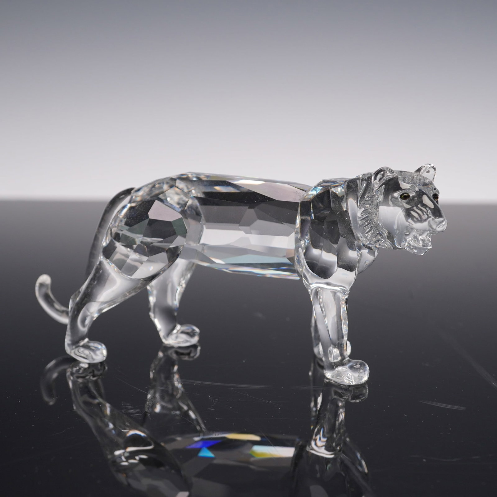 Swarovski Crystal Figurine, Tiger: The piece is crafted in clear faceted crystal with detailed molded features, including a textured mane, expressive face, and curved tail. The figurine is presented with its original Swarovski box and 